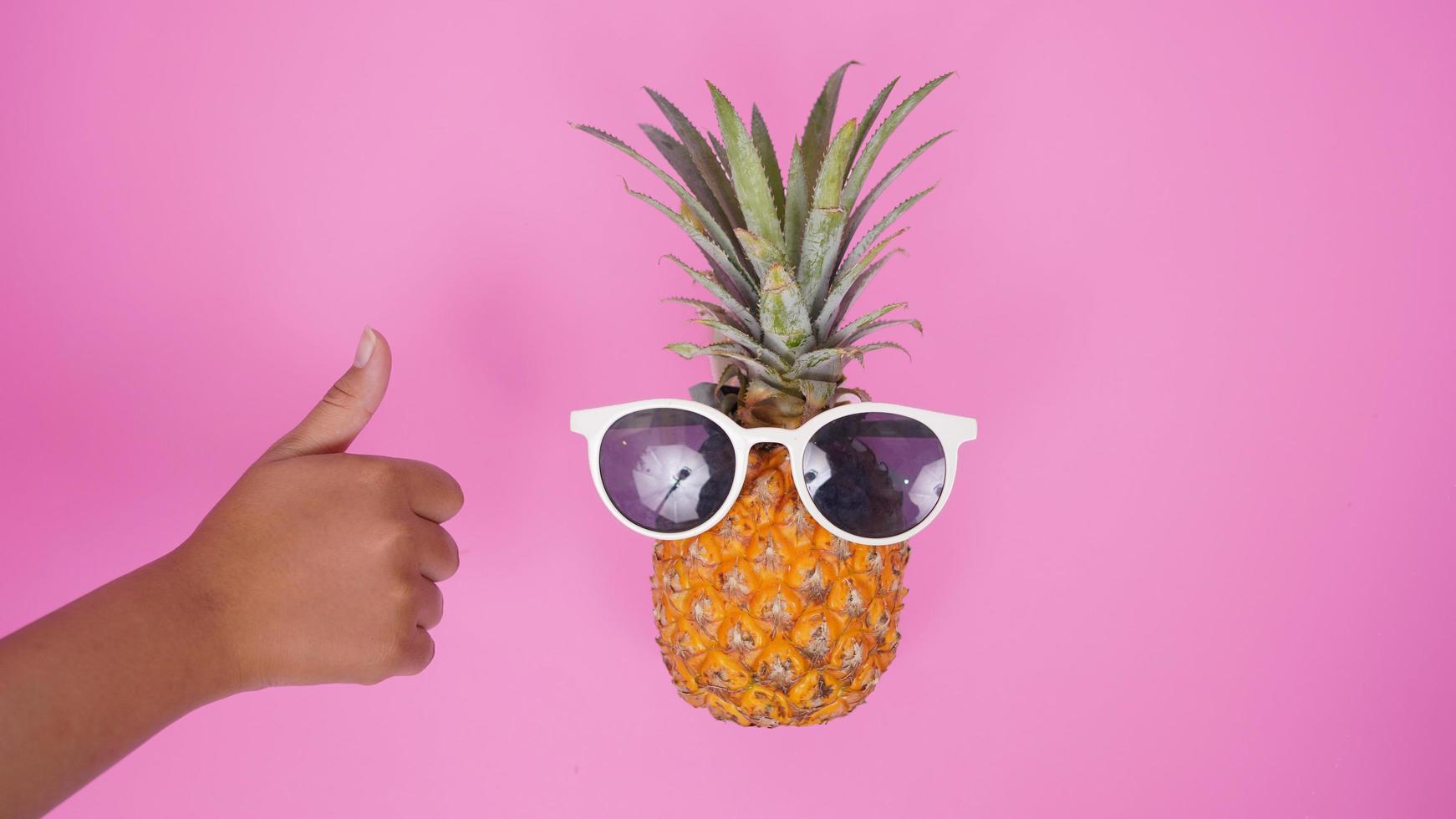 ananas frukt med glasögon och tummen isolerad på rosa bakgrund foto