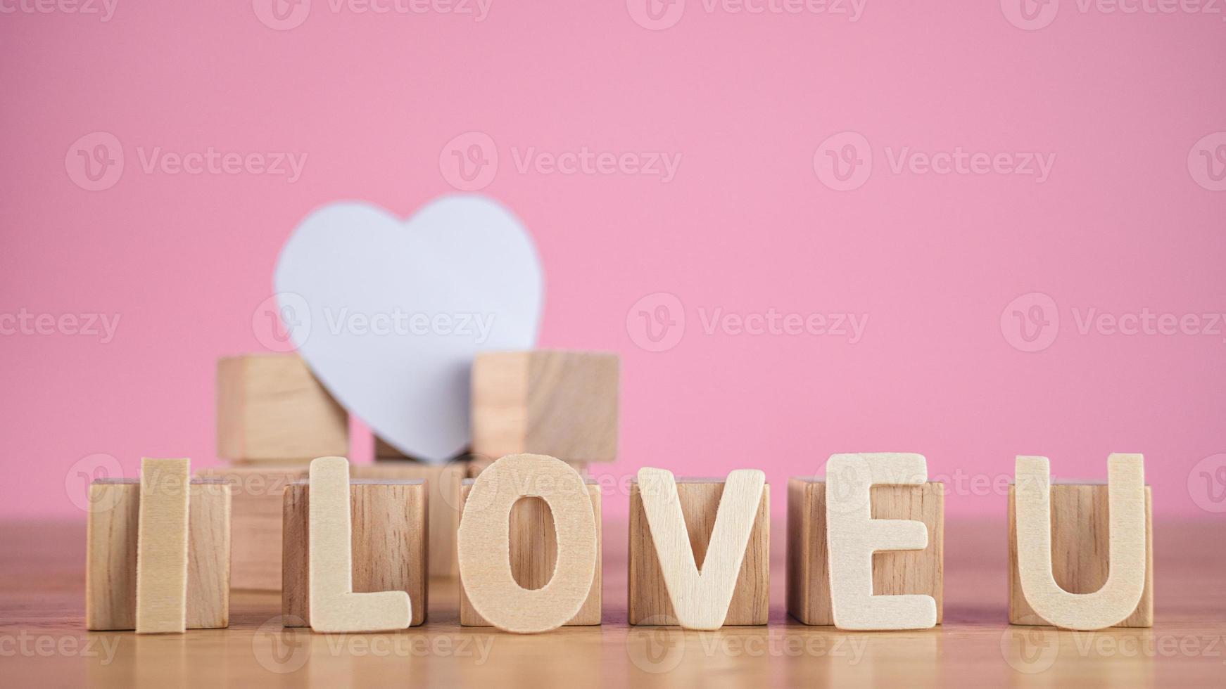 dessa ord betyder att jag älskar dig i trätallrikar. de fyrkantiga blocken stödjer det vita hjärtat. närbild skott isolerad på rosa bakgrund. alla hjärtans dag koncept. foto