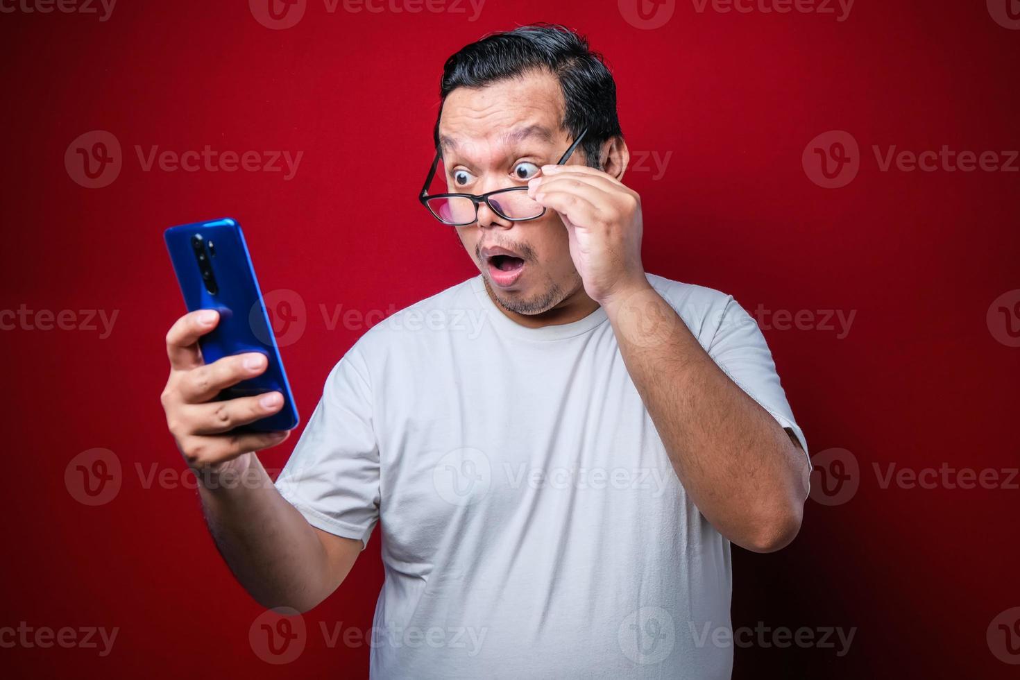 asiatisk kille som bär en vit t-shirt ser förvånad över de goda nyheterna han fick från sin smartphone. foto