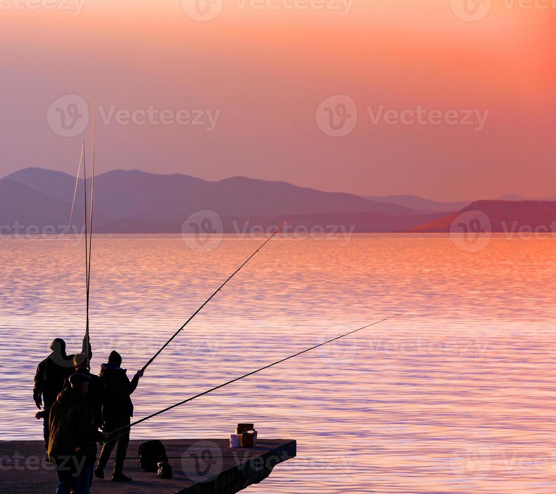 fishermanes siluett fiske vid solnedgången på sjön foto