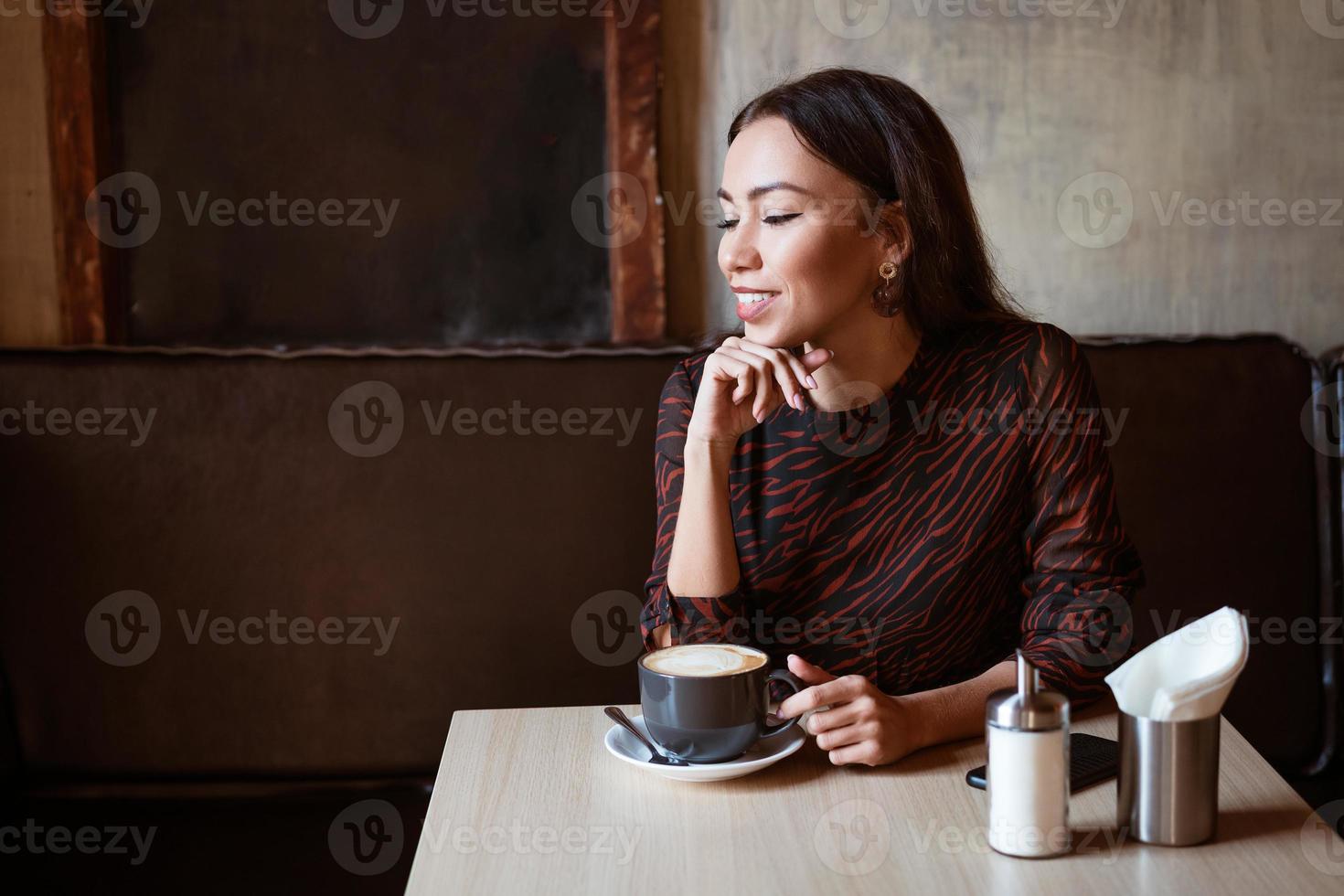 glad flicka vid ett bord på ett café med en kopp kaffe foto