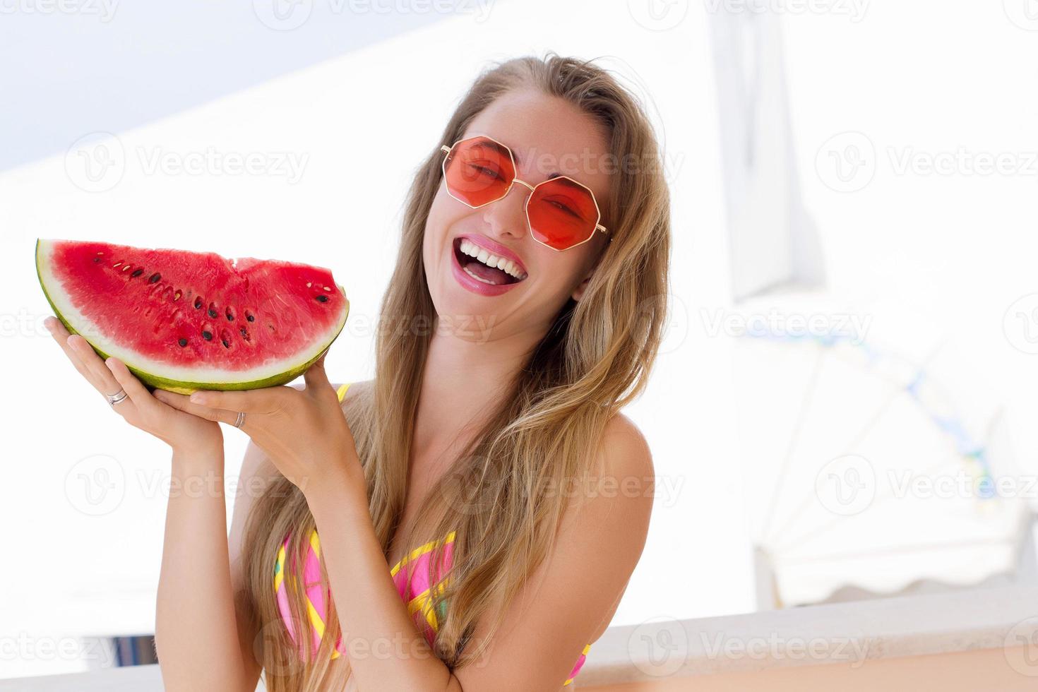 närbild av glad tjej i rosa solglasögon och vattenmelon frukt. sommarlov och rolig helg. sommartid koncept. leende ung kvinna i mode baddräkt. selektiv fokusering. strand sommar outfit. foto