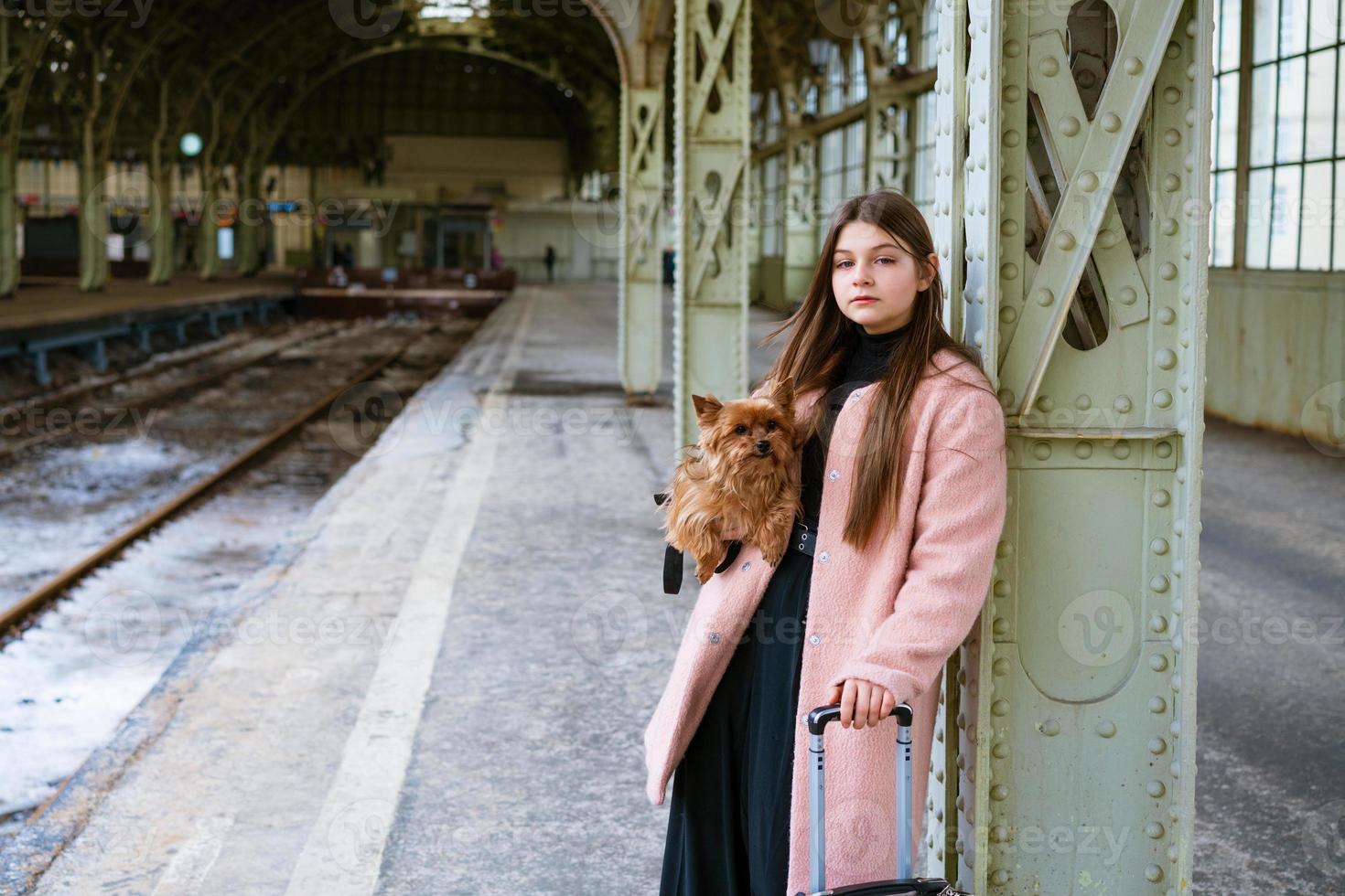vacker ung casual turist kvinna med hund och resväska väntar på tåg foto
