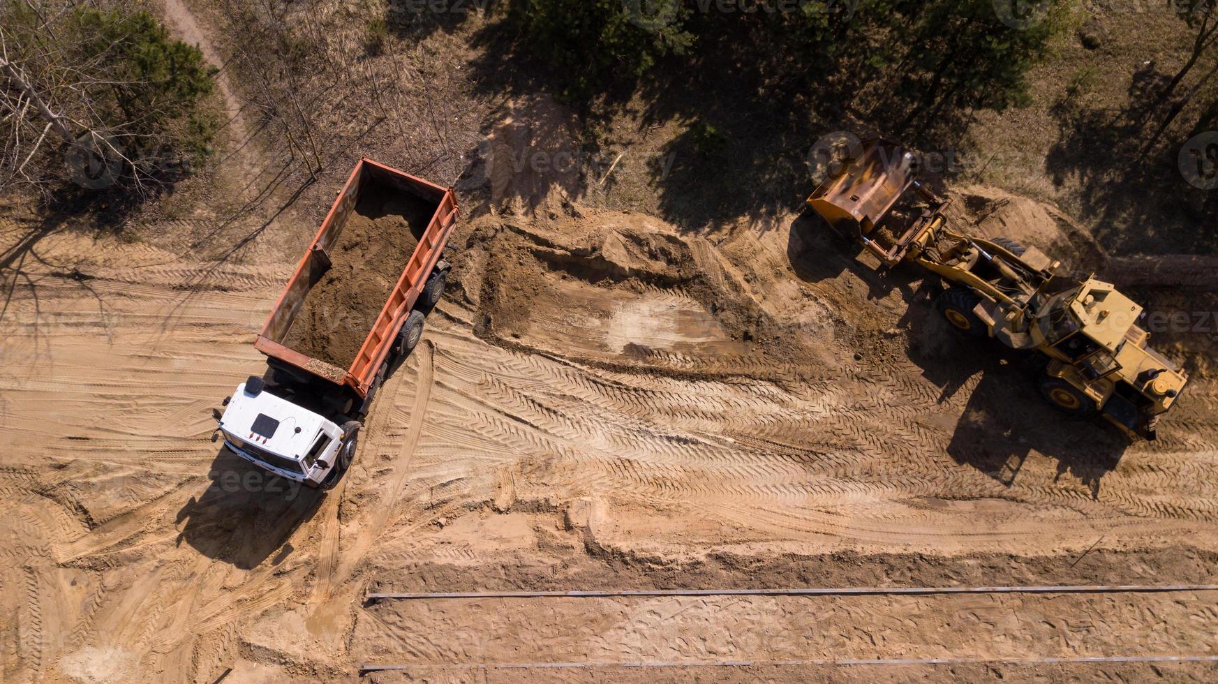 grävmaskin som lastar sand i en lastbil med flygfotograferingsdrönare foto