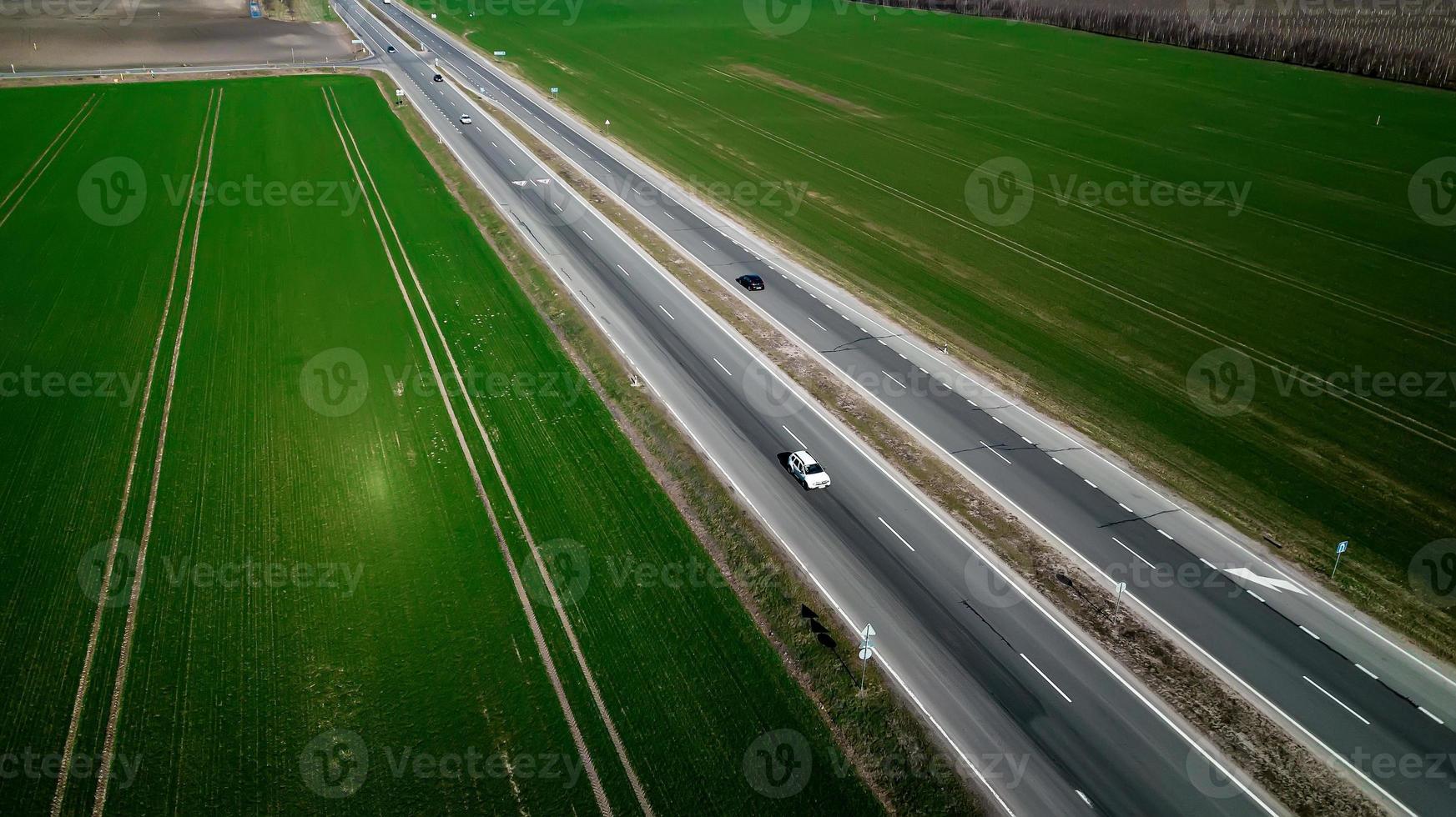 Flygbild över trafiken på tvåfilig väg genom landsbygd och odlade fält foto