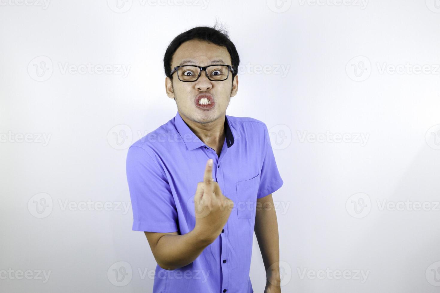 ung asiatisk man bär blå skjorta är ett roligt argt ansikte med att skrika och peka finger mot kameran isolerad över vit bakgrund foto