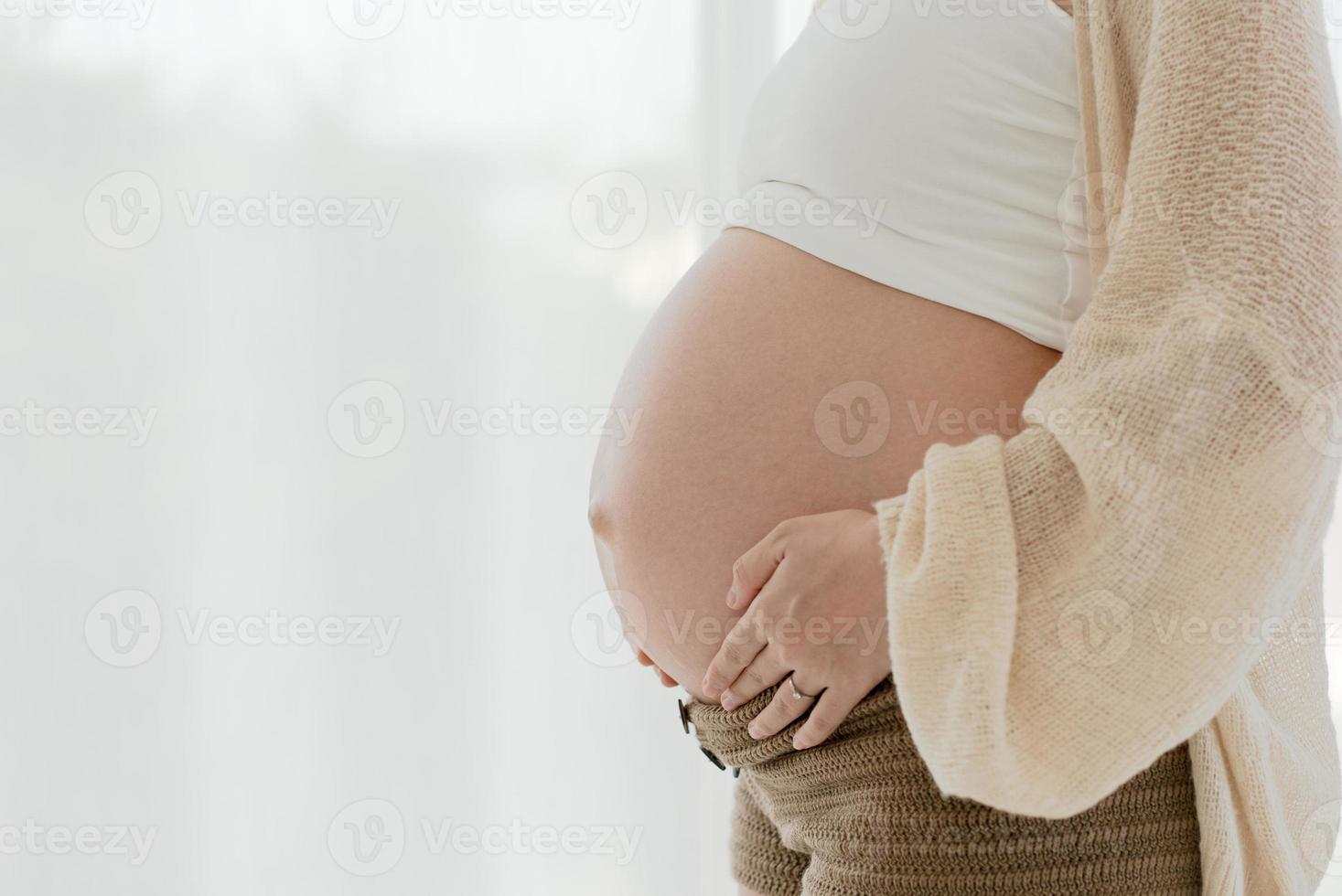 porträtt av gravid kvinna röra magen och stå vid fönstret foto