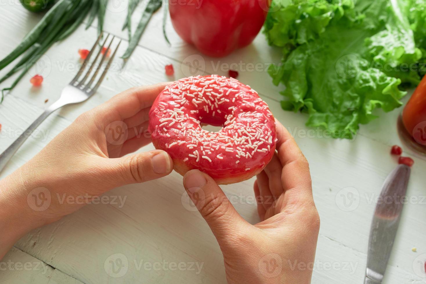 kvinnliga händer håller en välsmakande munk på en bakgrund av grönsaker. frestelsen att banta foto