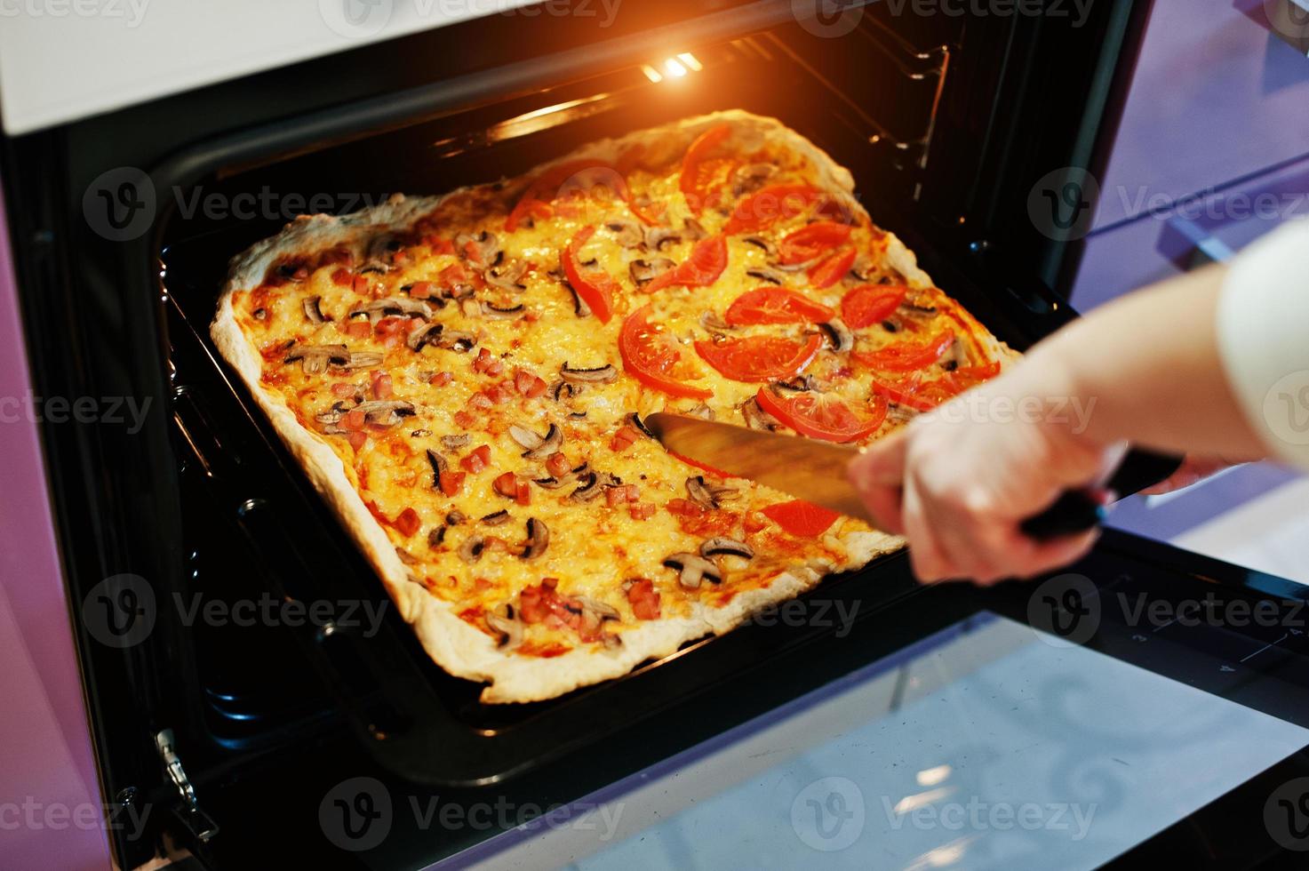 kvinna skär med en kniv hemlagad pizza i elektrisk ugn i köket foto