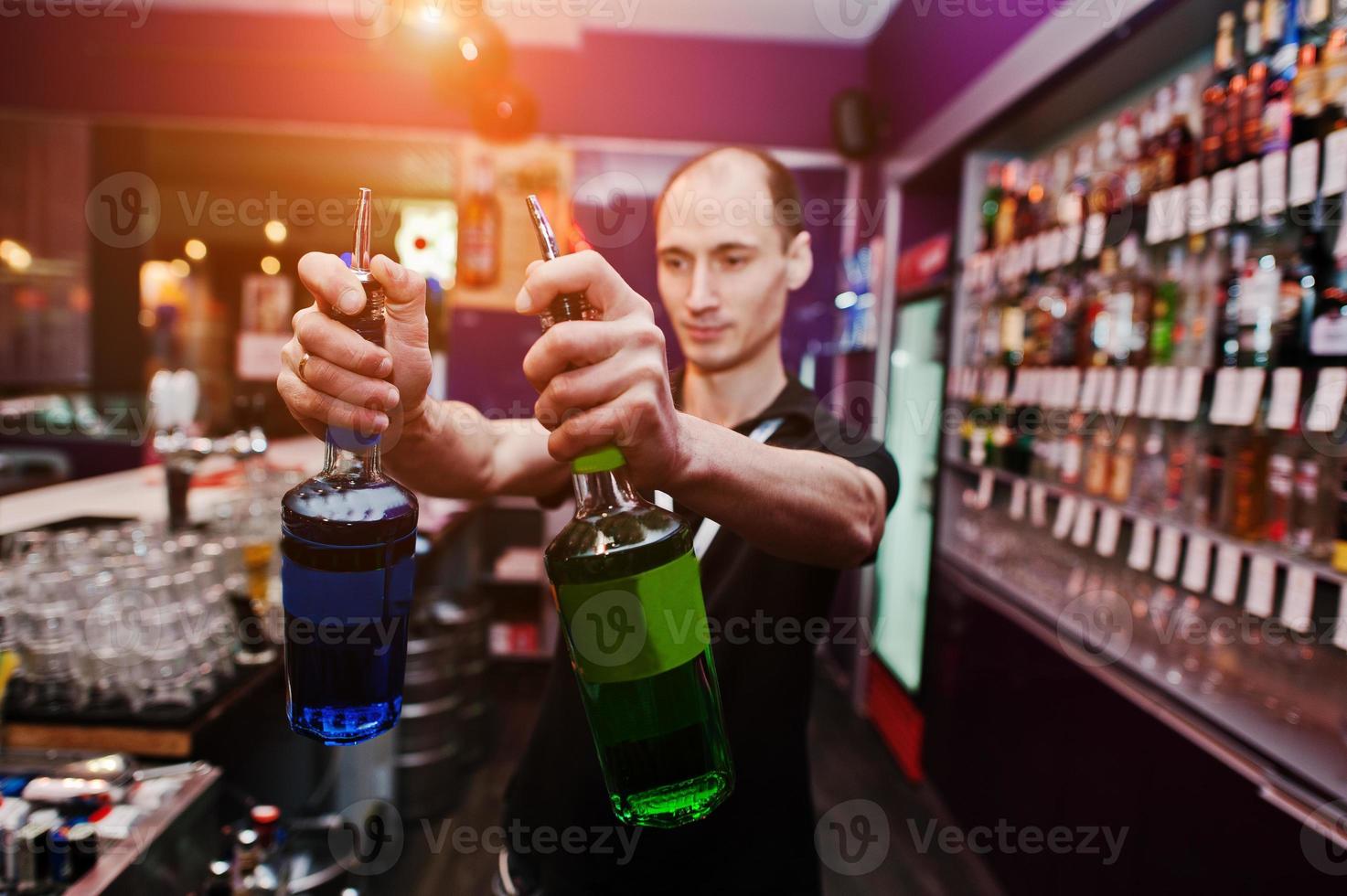 ung barman håller flaskor för cocktail i baren foto