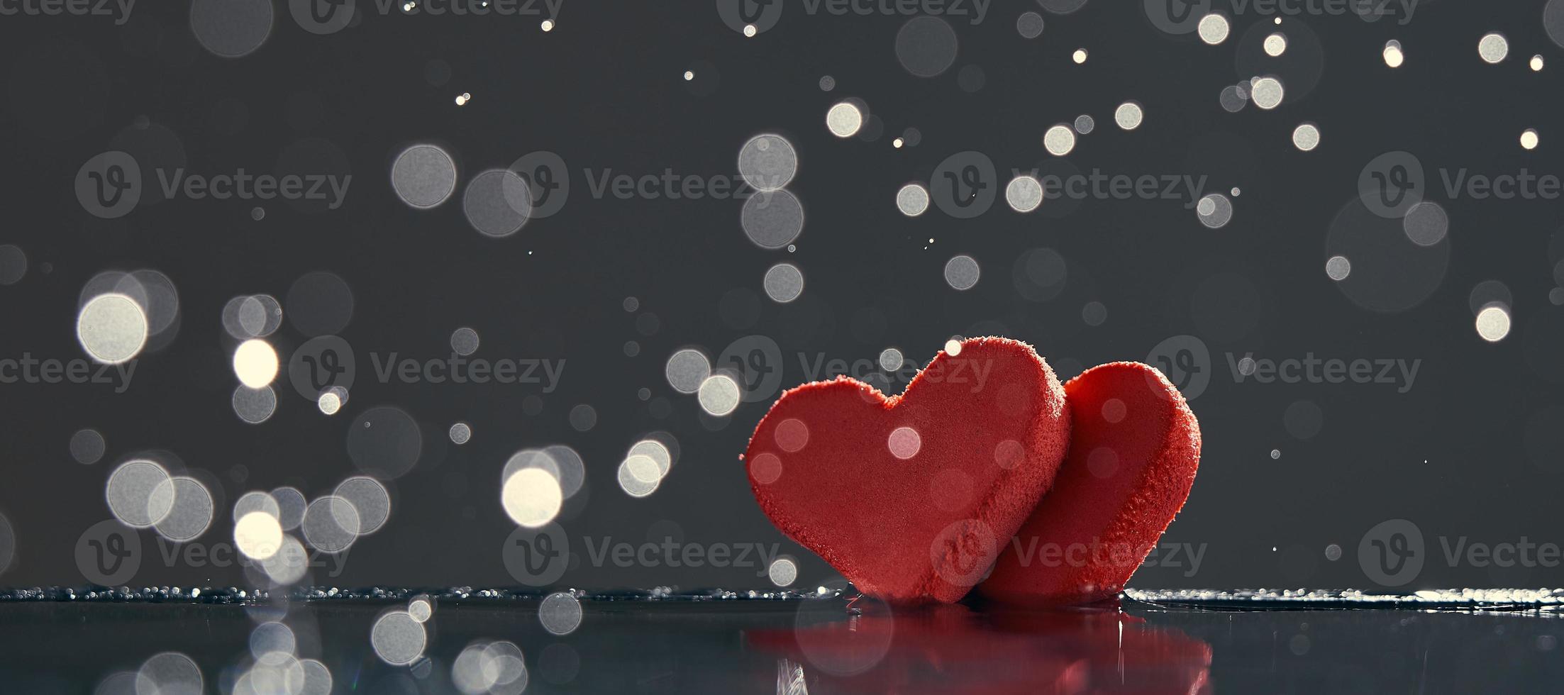 två röda hjärtan med regndroppar upplysta av varmt ljus på mörk bakgrund med en bokeh. foto med kopia utrymme.