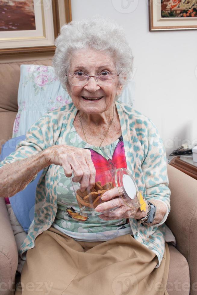 äldre dam hemma håller en burk kakor i handen foto