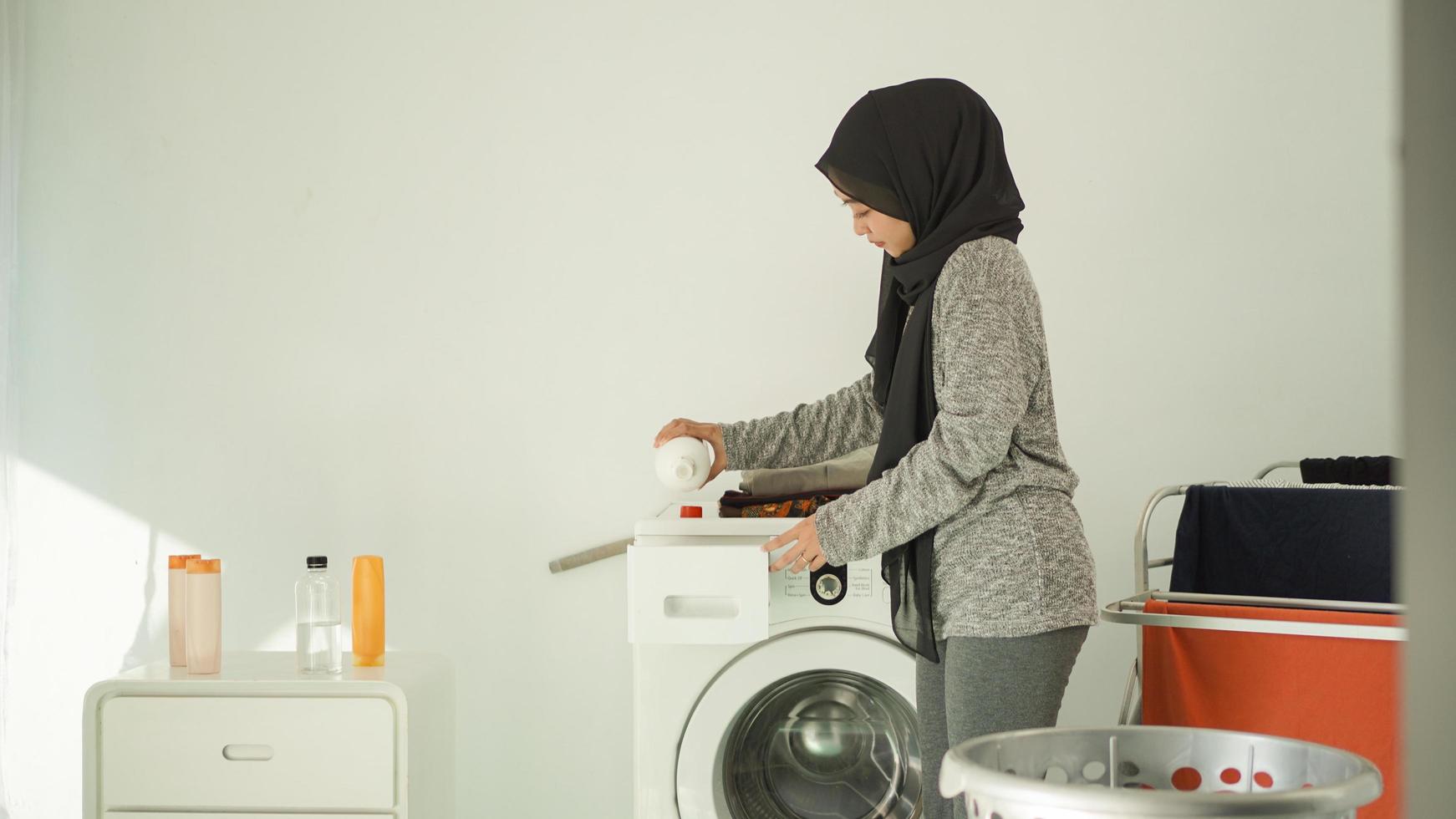 vacker kvinna i hijab häller tvättmedel för sin tvätt hemma foto
