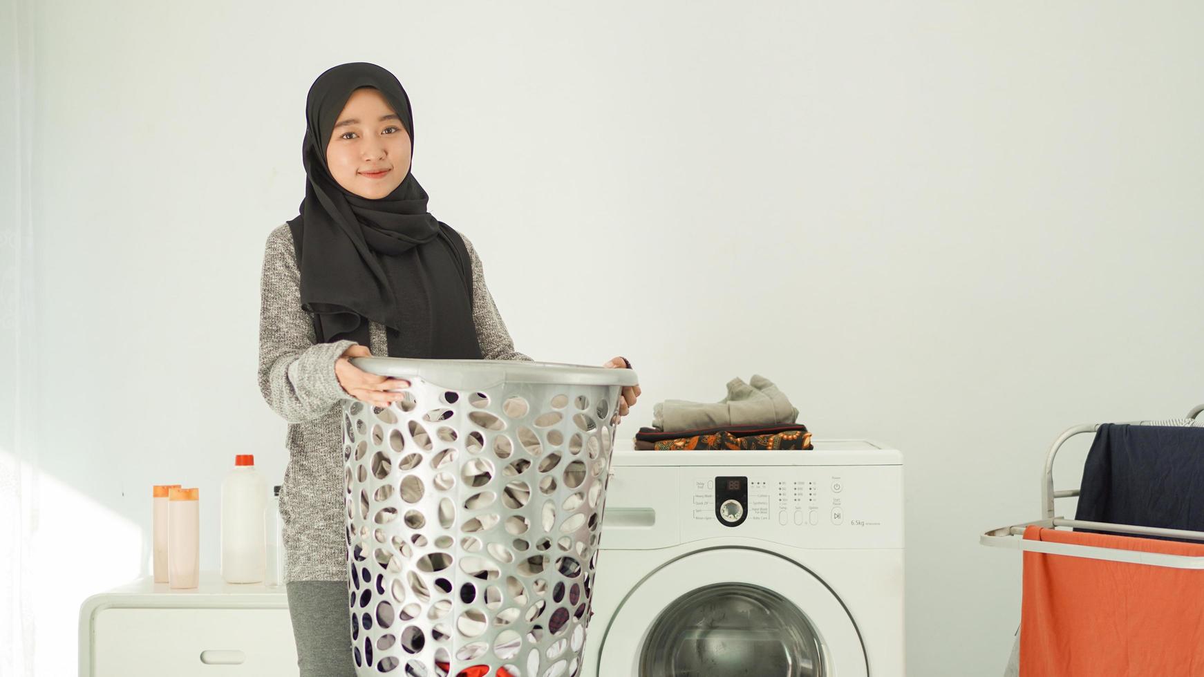 asiatisk kvinna i hijab tar med sig en korg med kläder att tvätta hemma foto