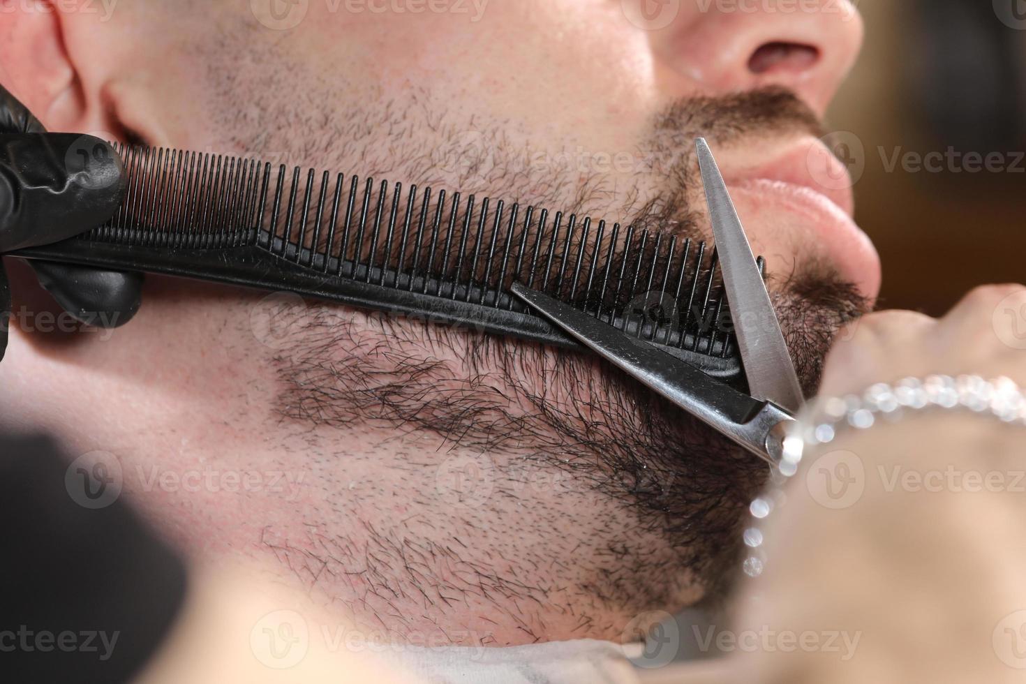 frisyr av en mans skägg i en frisörsalong. professionell mästerbarberare rakar kundens skägg med en sax. frisör män. reklam och frisersalong koncept. selektiv fokusering foto