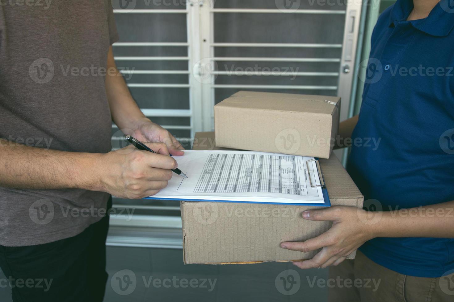 leverans ung man som står vid dörren till hemmet och bär paket för ung man att signera. foto