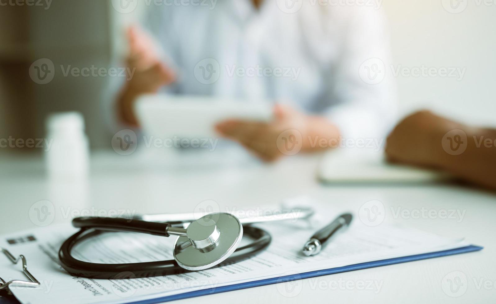 Närbildsstetoskop och läkare pratar med patienten på kliniken medan du använder tabletten och förklarar patientens tillstånd och behandlingsresultatet. foto