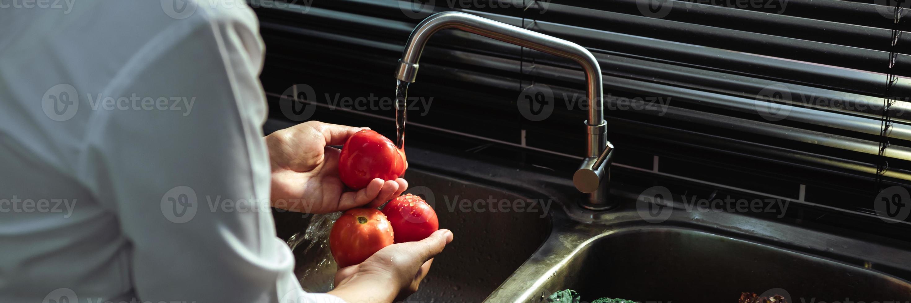 asiatiska händer kvinna tvätta grönsaker tomat och förberedelse hälsosam mat i köket. foto