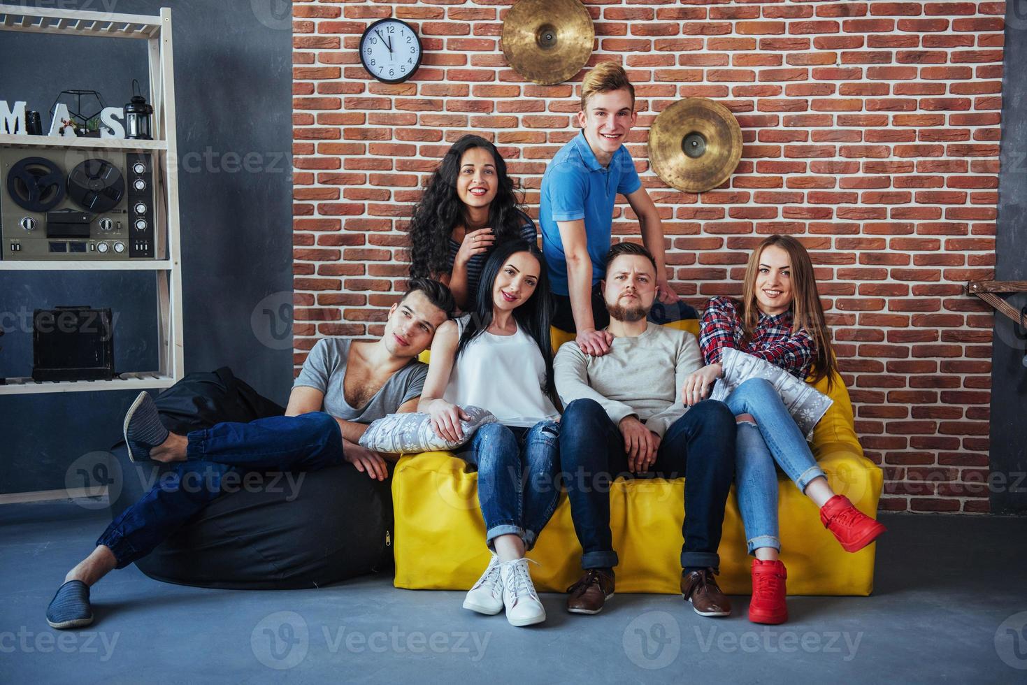 gruppporträtt av multietniska pojkar och flickor med färgglada moderiktiga kläder som håller en vän som poserar på en tegelvägg, människor i urban stil som har roligt, koncept om livsstil för ungdomars gemenskap foto