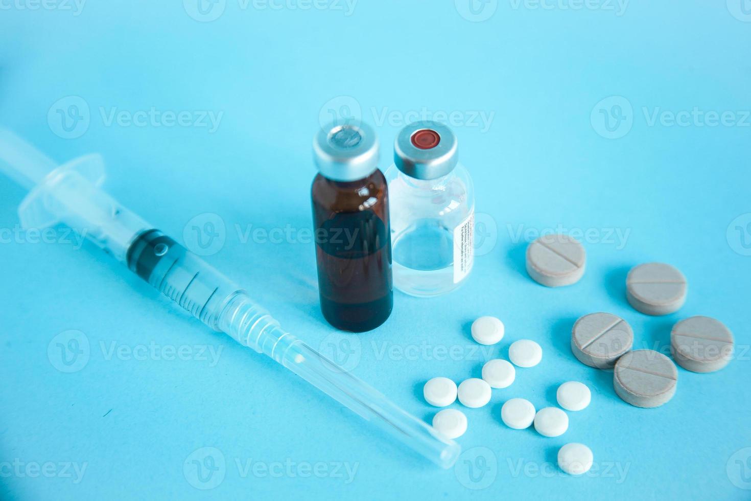 närbild av medicinsk ampull, spruta och piller isolerad på blå bakgrund foto