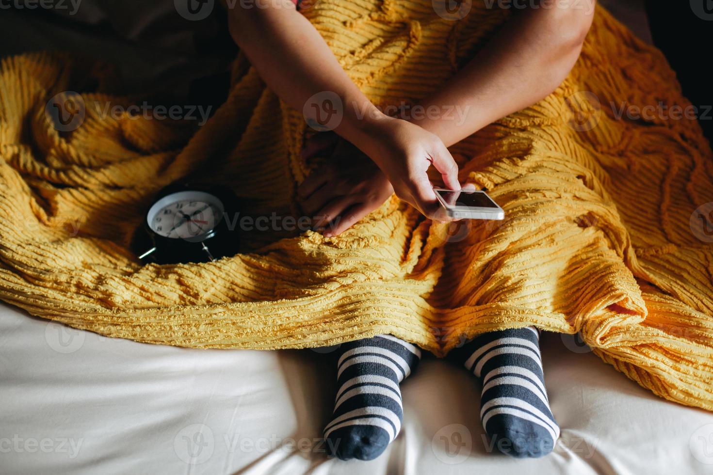 ett folk under filtar bär strumpor på sängen och använder smart telefon foto