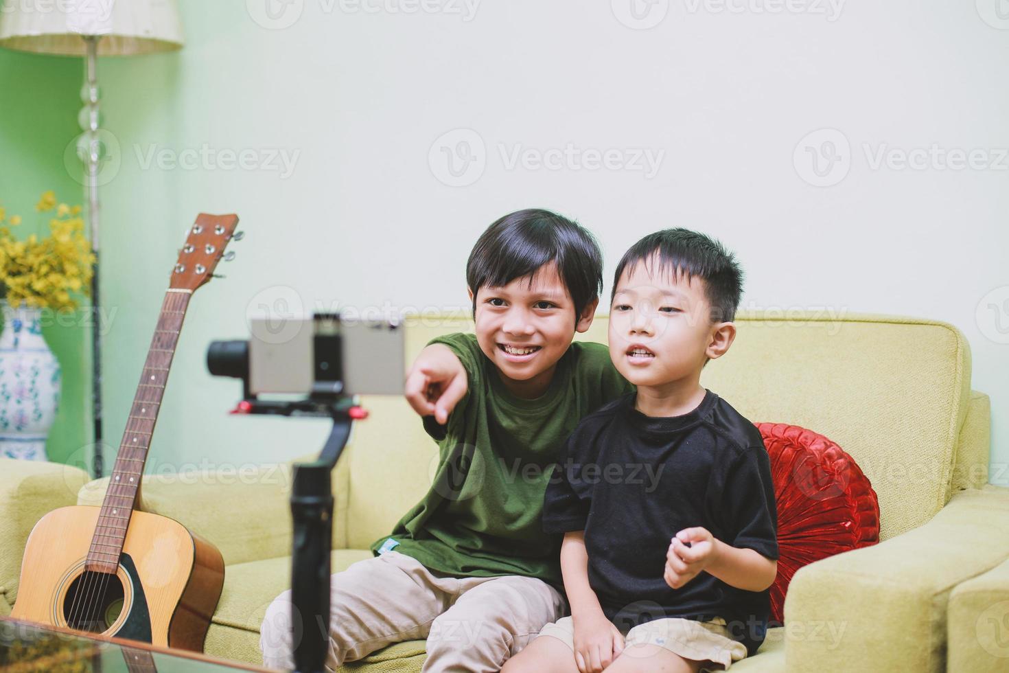 två asiatiska barn-youtuber som ler och interagerar med sin publik på telefonen medan de streamar live foto