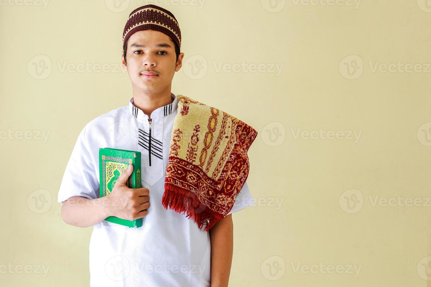 porträtt av ung asiatisk muslim som håller den heliga boken al-Koranen och bönemattan på axeln gör dig redo att be foto
