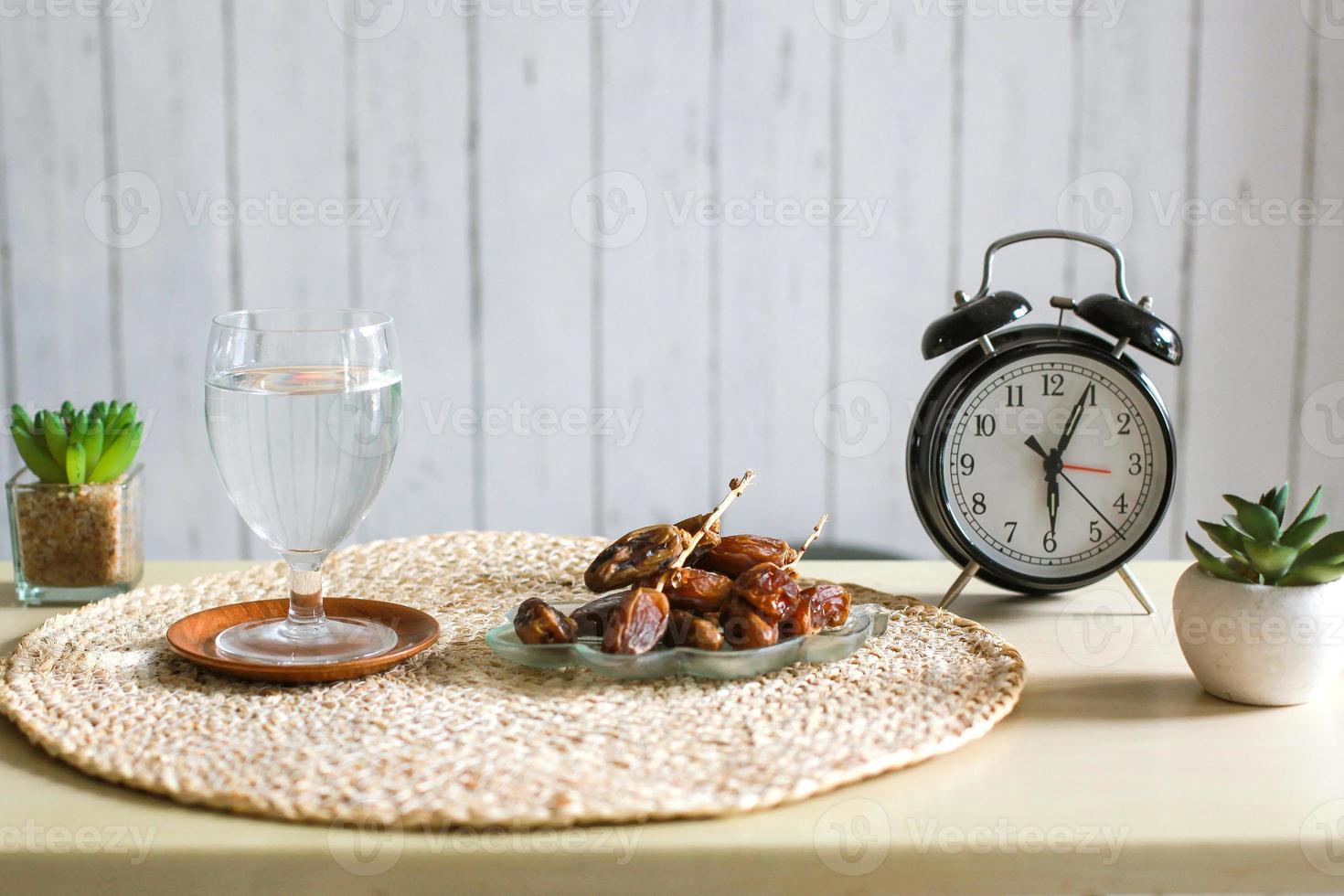 glas dricksvatten och dadlar med väckarklocka som visar klockan 6. traditionell ramadan, iftar tidskoncept foto
