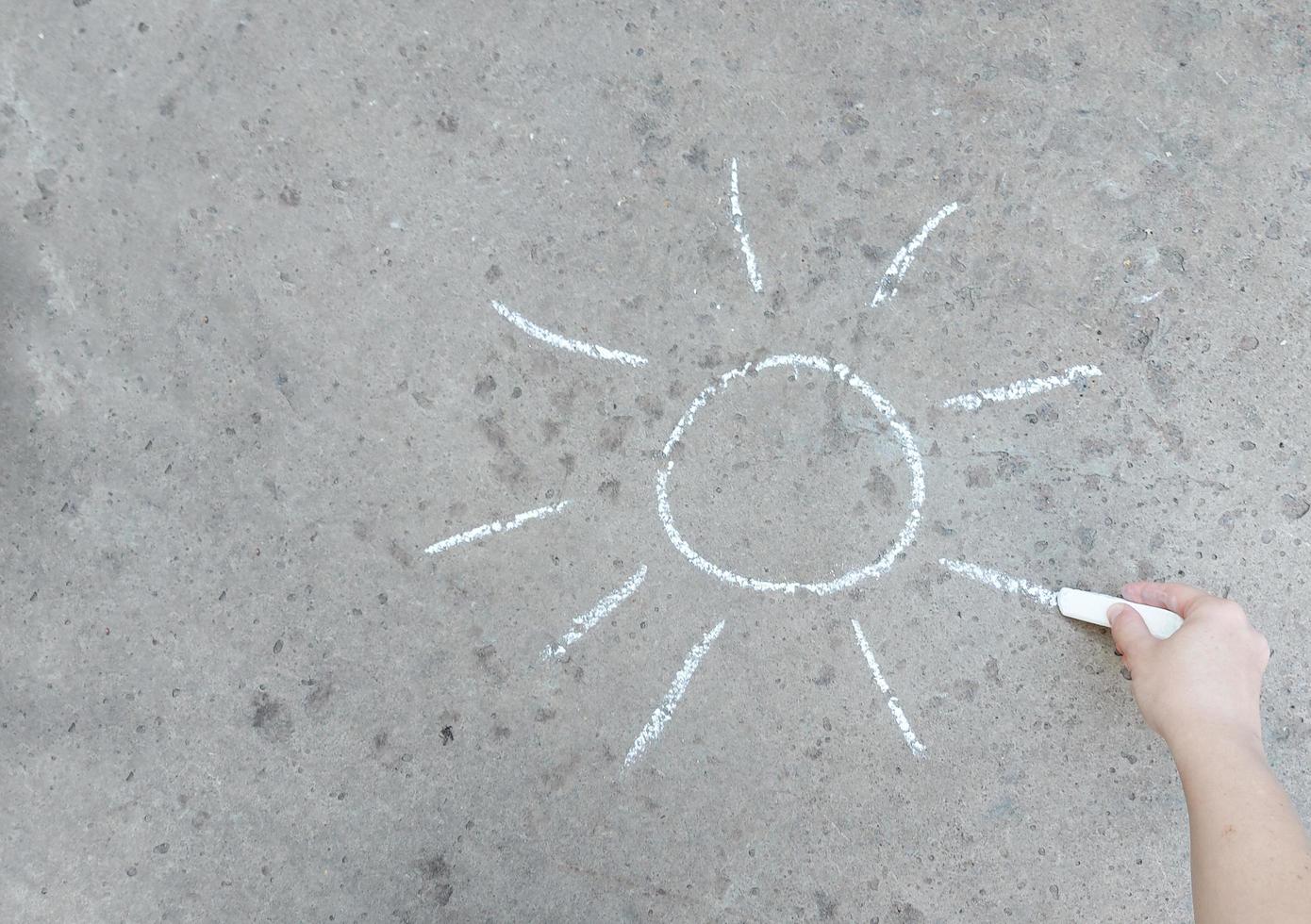 handen ritar solen på trottoaren med krita. kreativitet, sommar, kreativitet. kopiera utrymme, plats för text. foto