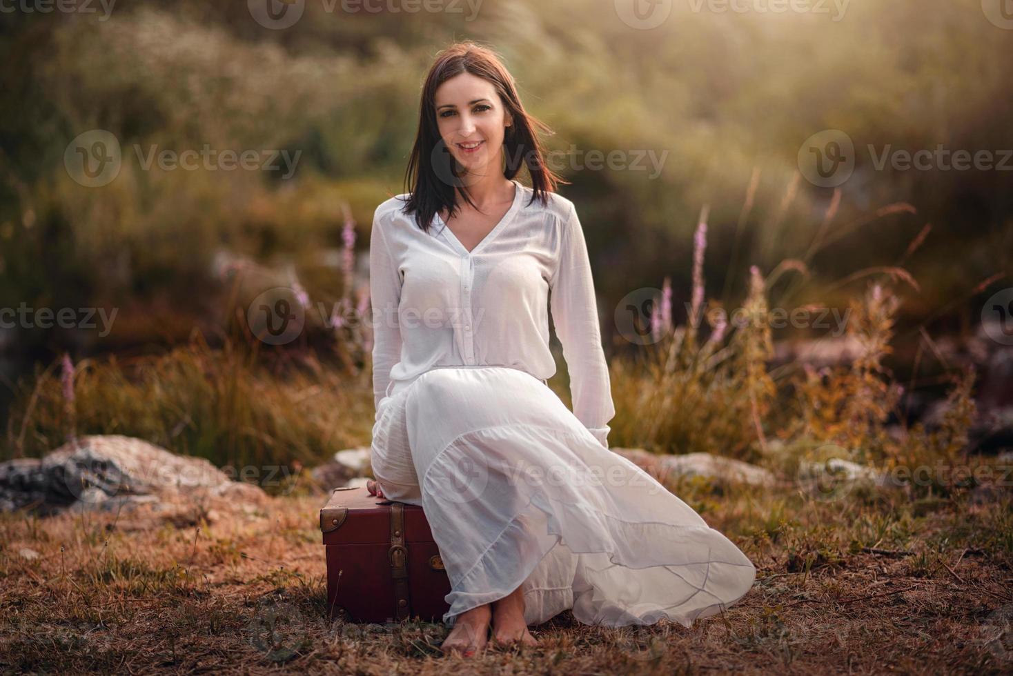 ung kvinna sitter på fältet med resväska foto
