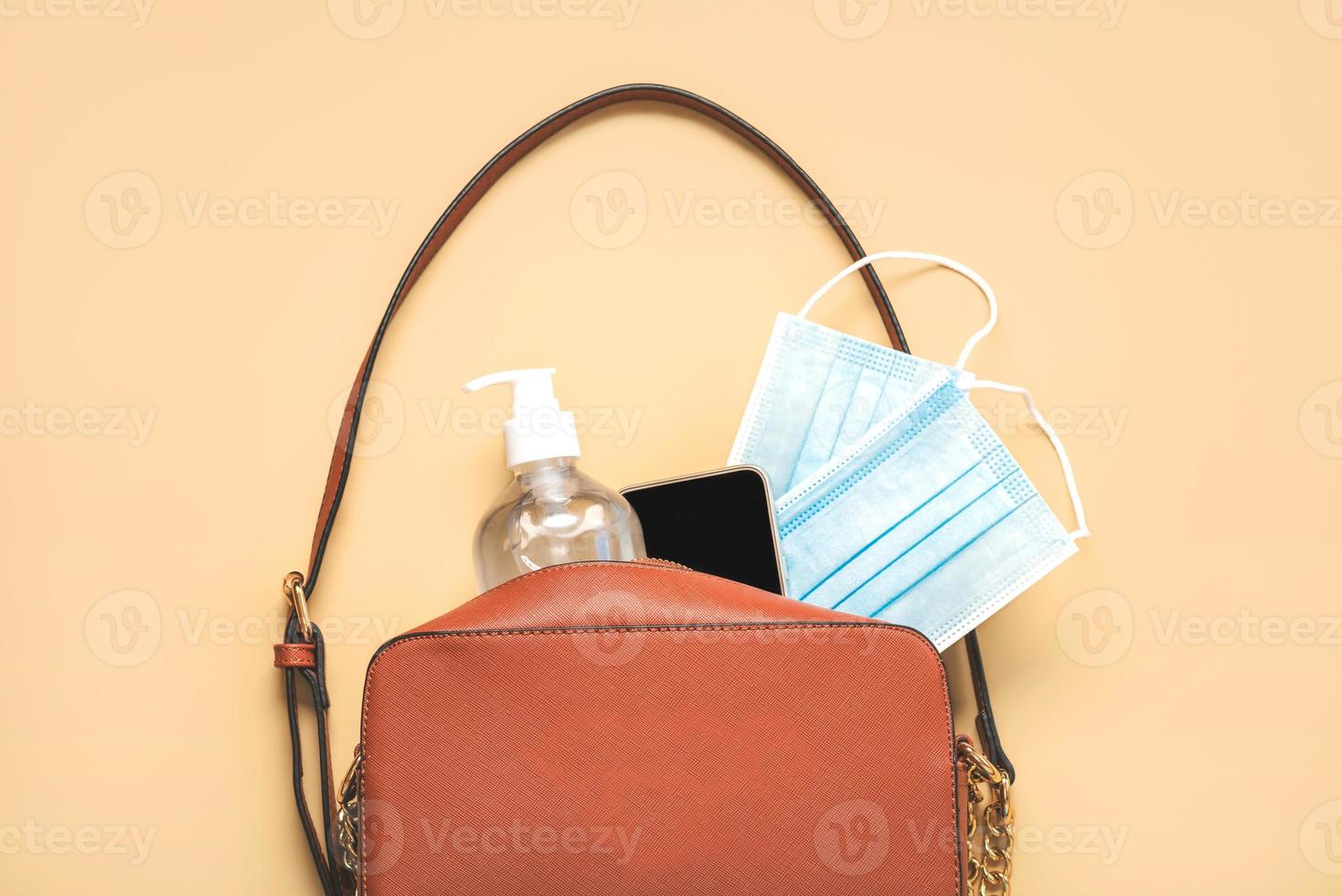 kvinnas väska med skyddande kirurgisk mask, desinficeringsflaska och smartphone.covid 19 koncept foto