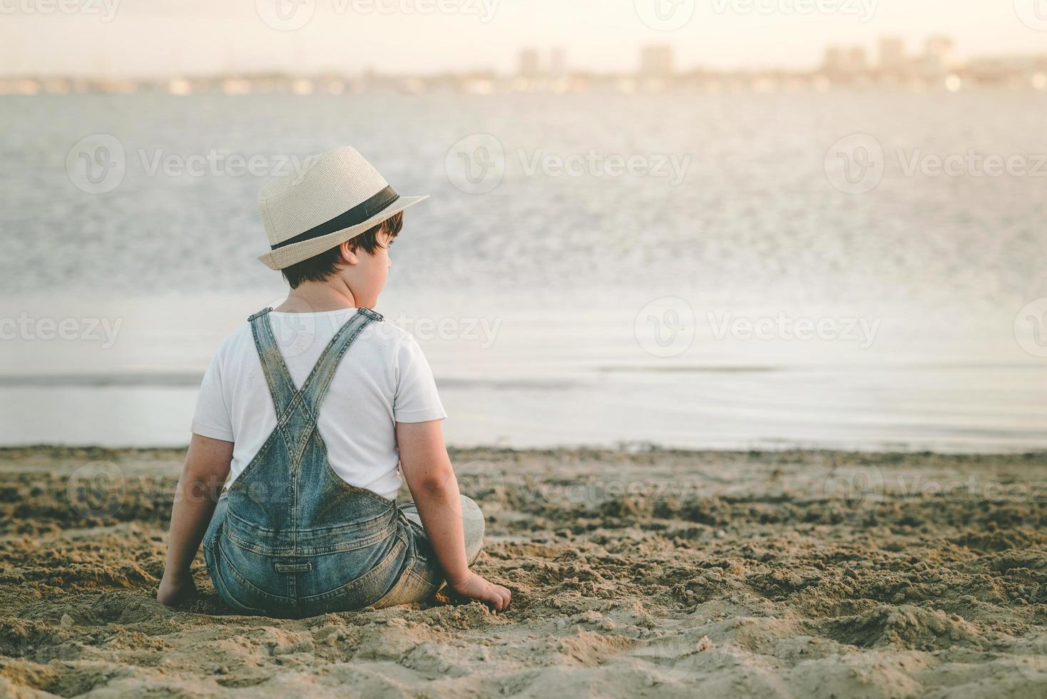 bakifrån av ett eftertänksamt barn som sitter på stranden foto