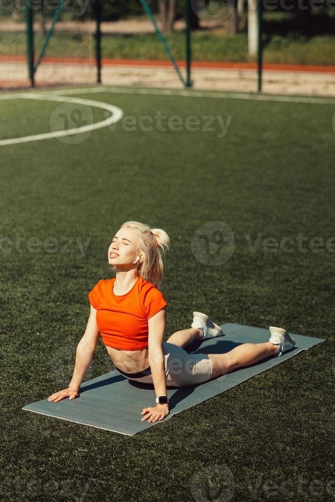 vacker blondin gör stretching på gräsmattan på en fotbollsplan foto