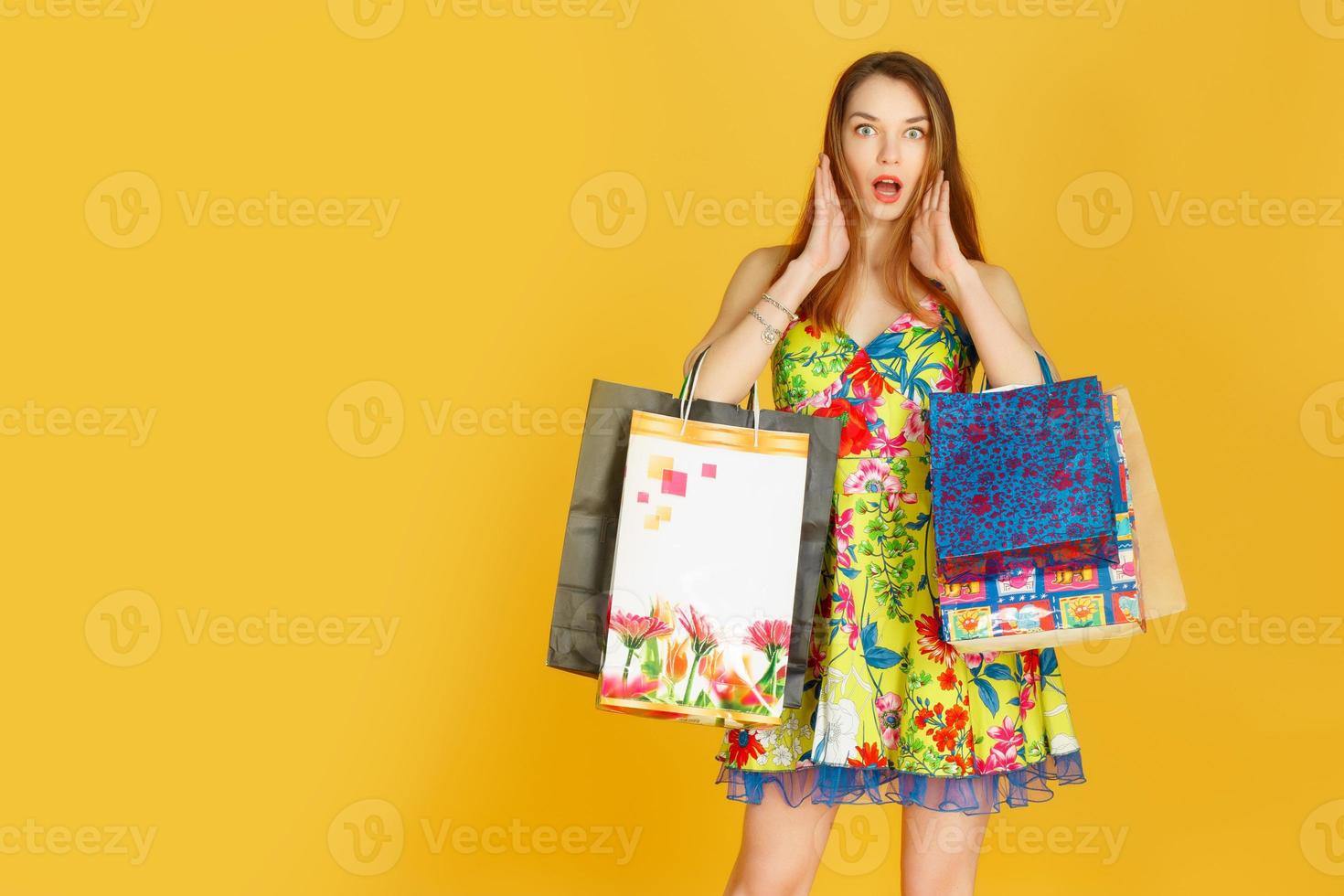 porträtt av ung glad leende kvinna med shoppingkassar mot gul vägg foto