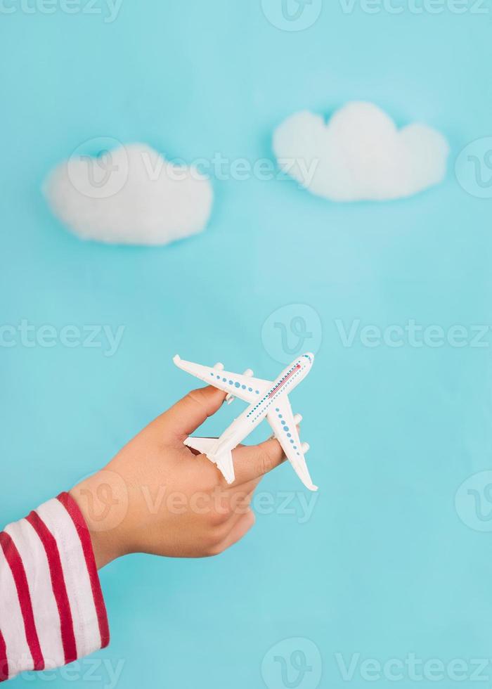 barnhänder som håller ett leksaksflygplan över moln. resekoncept foto