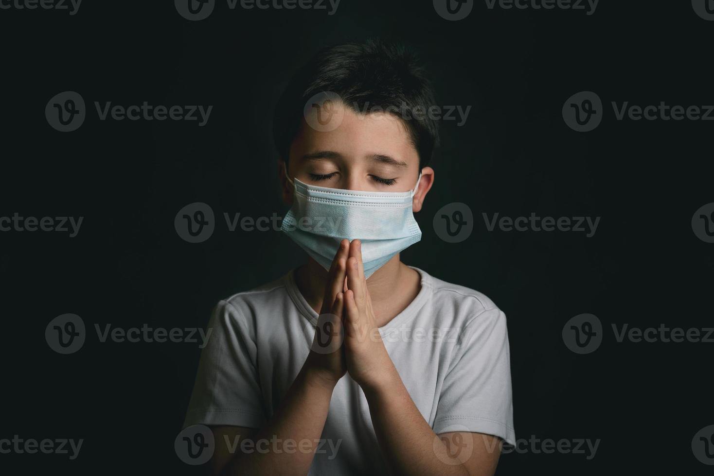 barn som bär medicinsk mask för coronavirus med händerna knäppta ihop och ber foto
