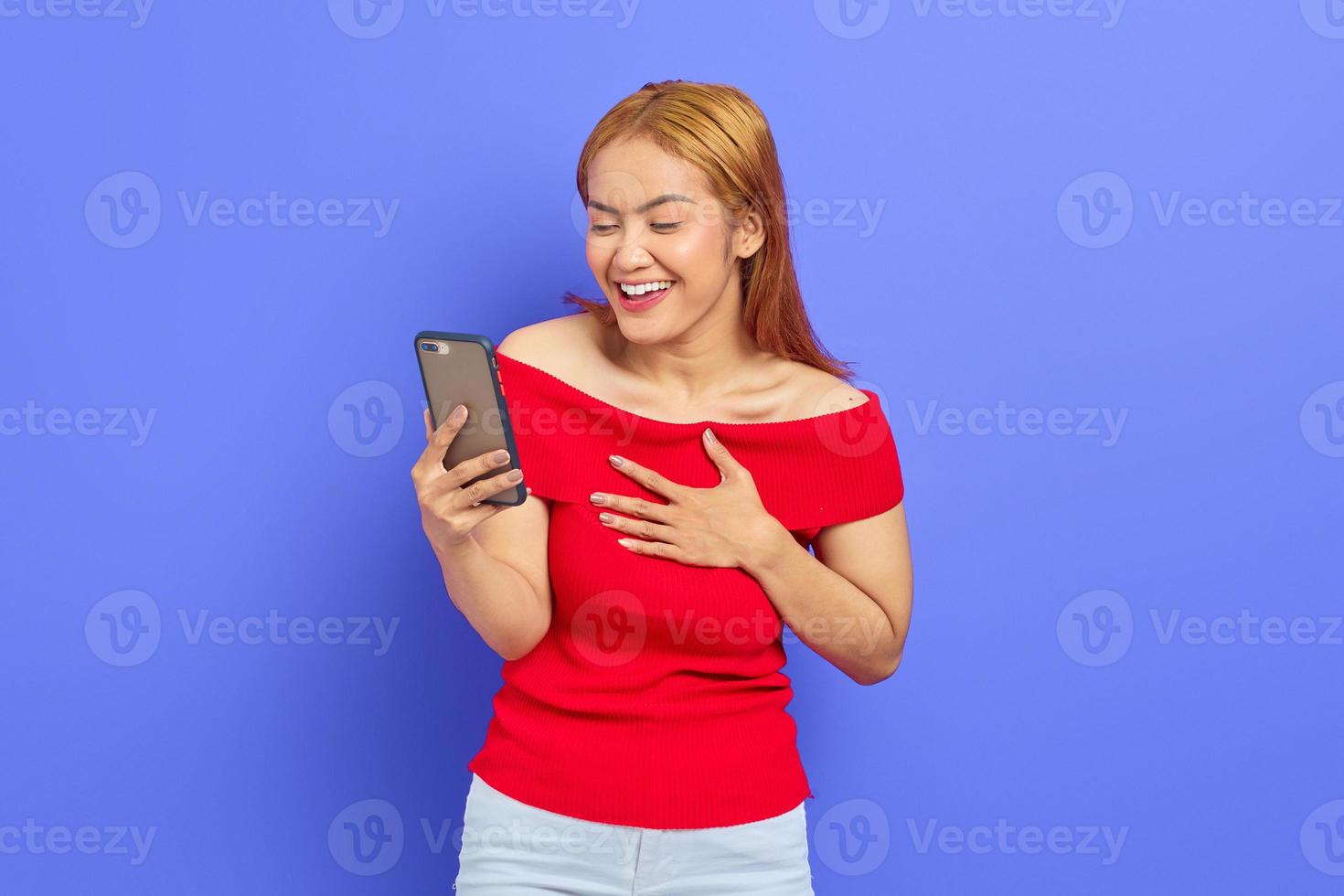 porträtt av upphetsad ung asiatisk kvinna som använder mobiltelefon isolerad på lila bakgrund foto