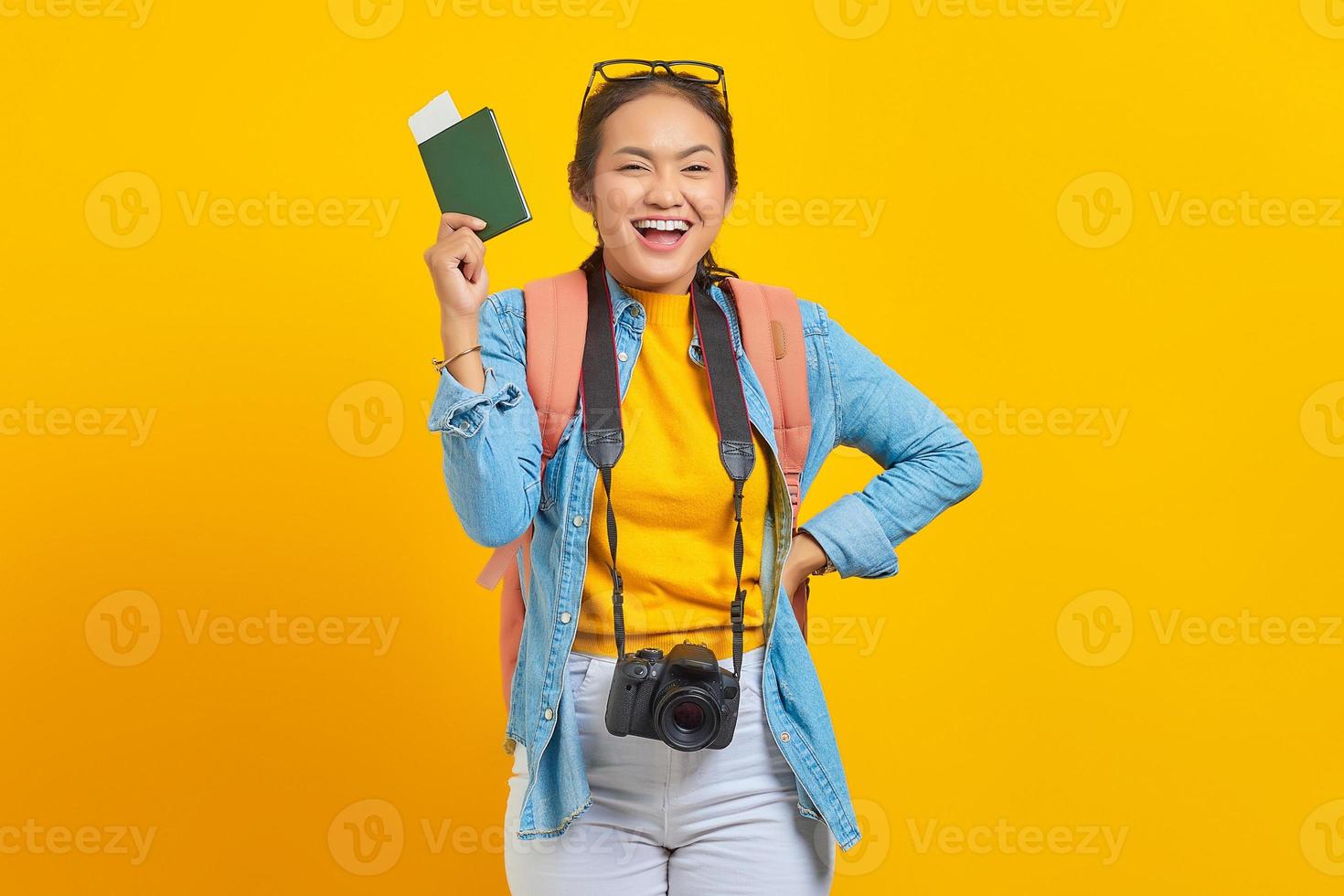 porträtt av glada unga asiatiska resenären håller pass boardingkort biljett isolerad på gul bakgrund. passagerare som reser på helger. flygresor koncept foto