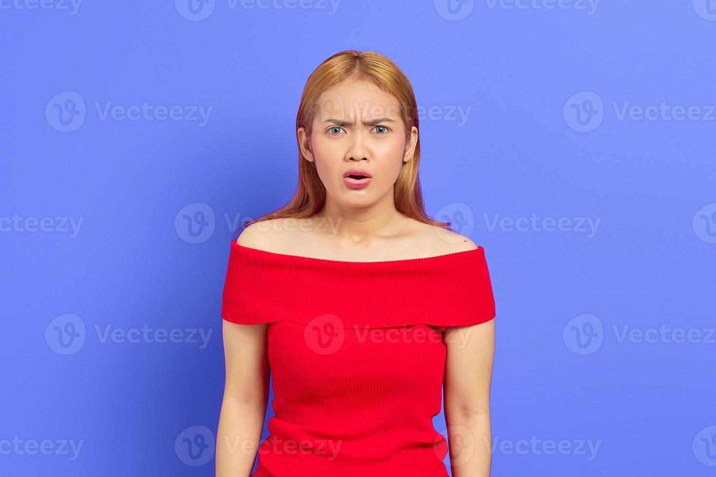 porträtt av vacker kvinna i röd klänning tittar på kameran med allvarligt ansikte och förvånad över att se något sällsynt på lila bakgrund foto