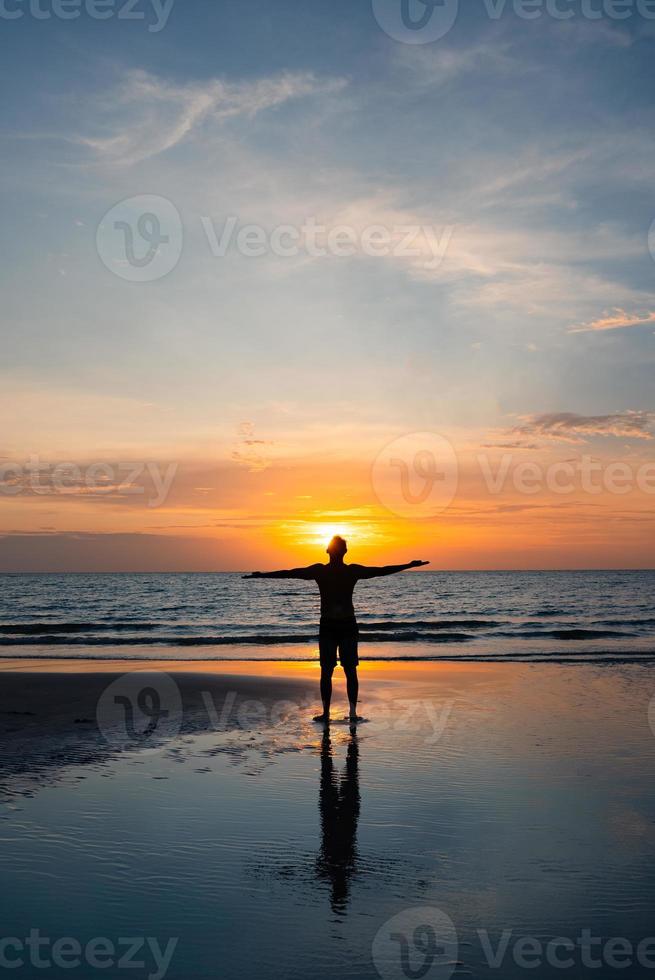siluett av mannen stanidng på stranden vid solnedgången foto
