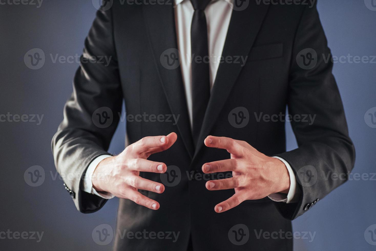 den unga affärsmannen i kostym visar sin hand på en isolerad mörk bakgrund foto