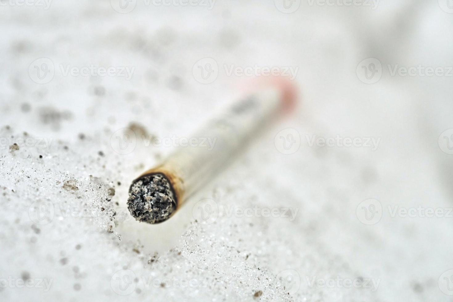 halvrökt cigarett liggande på snö makro foto