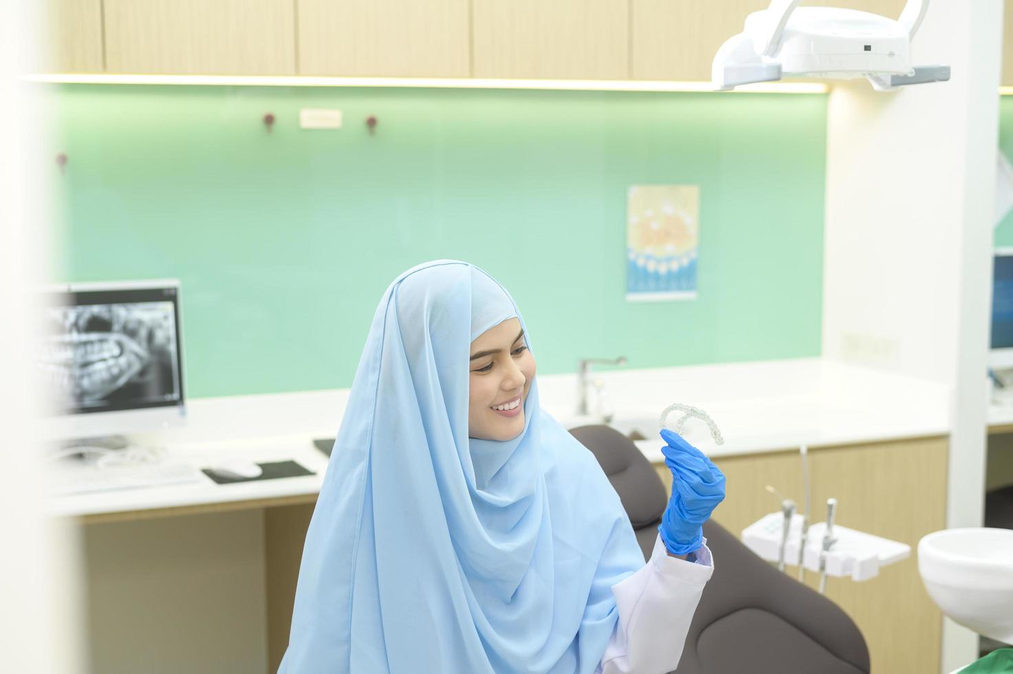 ung kvinnlig muslimsk tandläkare som håller invisalign på tandklinik, tandkontroll och koncept för friska tänder foto