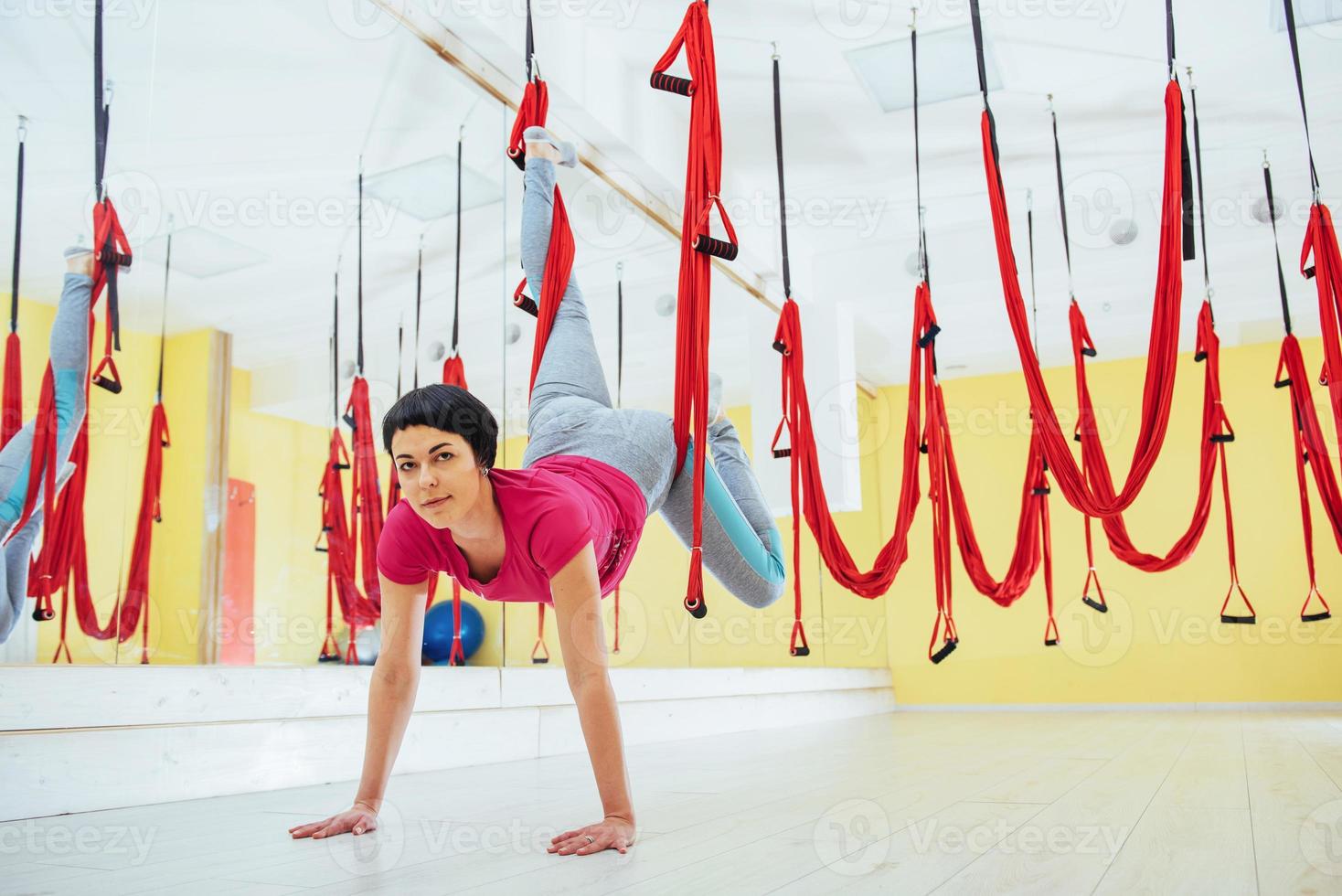 ung vacker kvinna utövar yogafluga med en hängmatta i den ljusa studion. flygning, kondition, stretch, balans, träning. foto