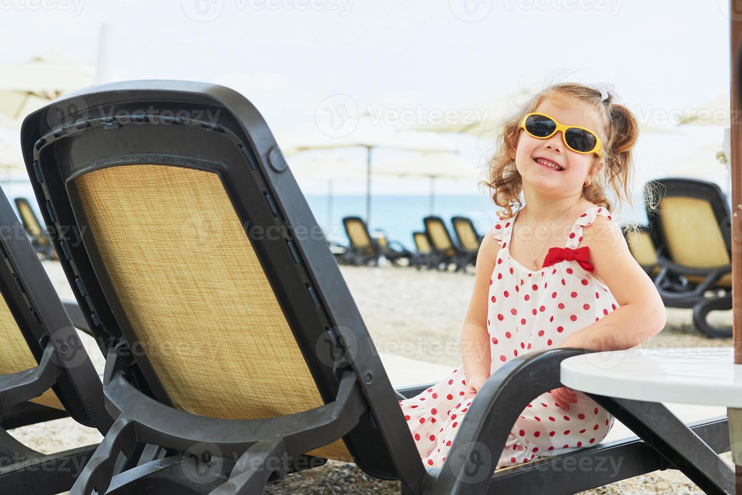 liten glad tjej på solstolarna vid havet, poserar för kameran foto