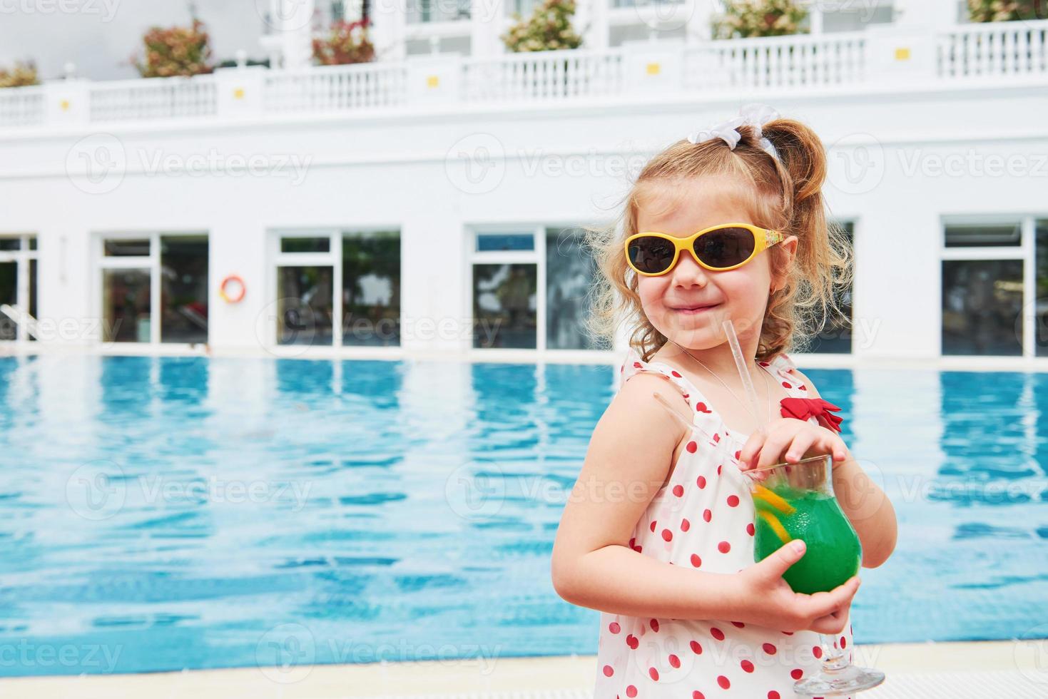 söt liten blondin vid poolen och håller ett barns cocktail foto