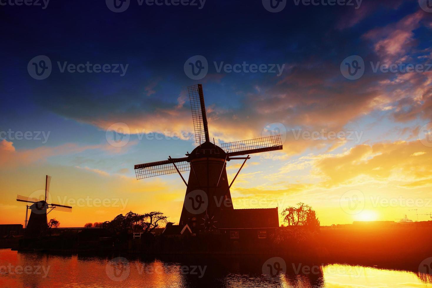 landskap med vacker traditionell holländsk kvarn nära vattendrag med fantastisk solnedgång och reflektion i vatten. nederländerna. foto