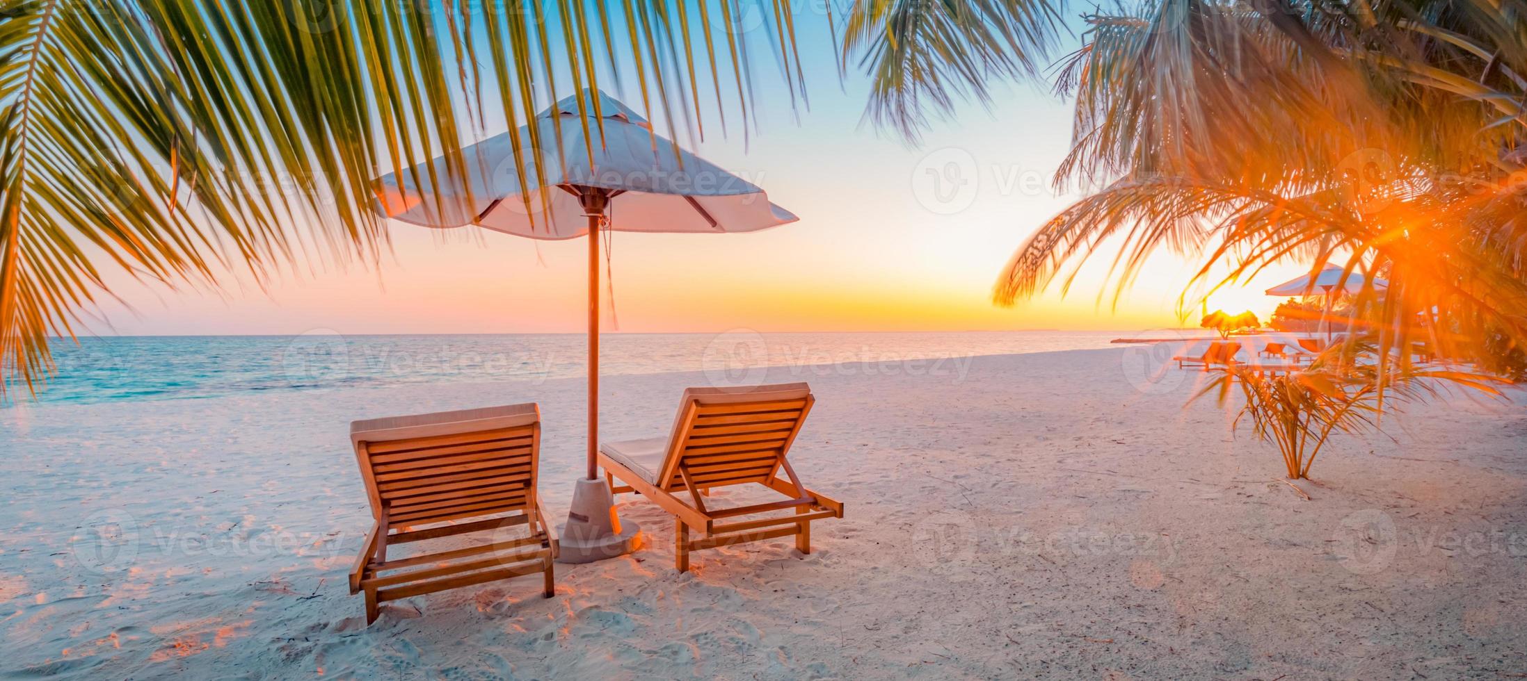 panoramautsikt tropisk strand solnedgång strålar, två solstolar, solstolar, parasoll under palmträd. vit sand, havshorisont, färgglad skymningshimmel, lugn slappna av banner. inspirerande strandhotell foto