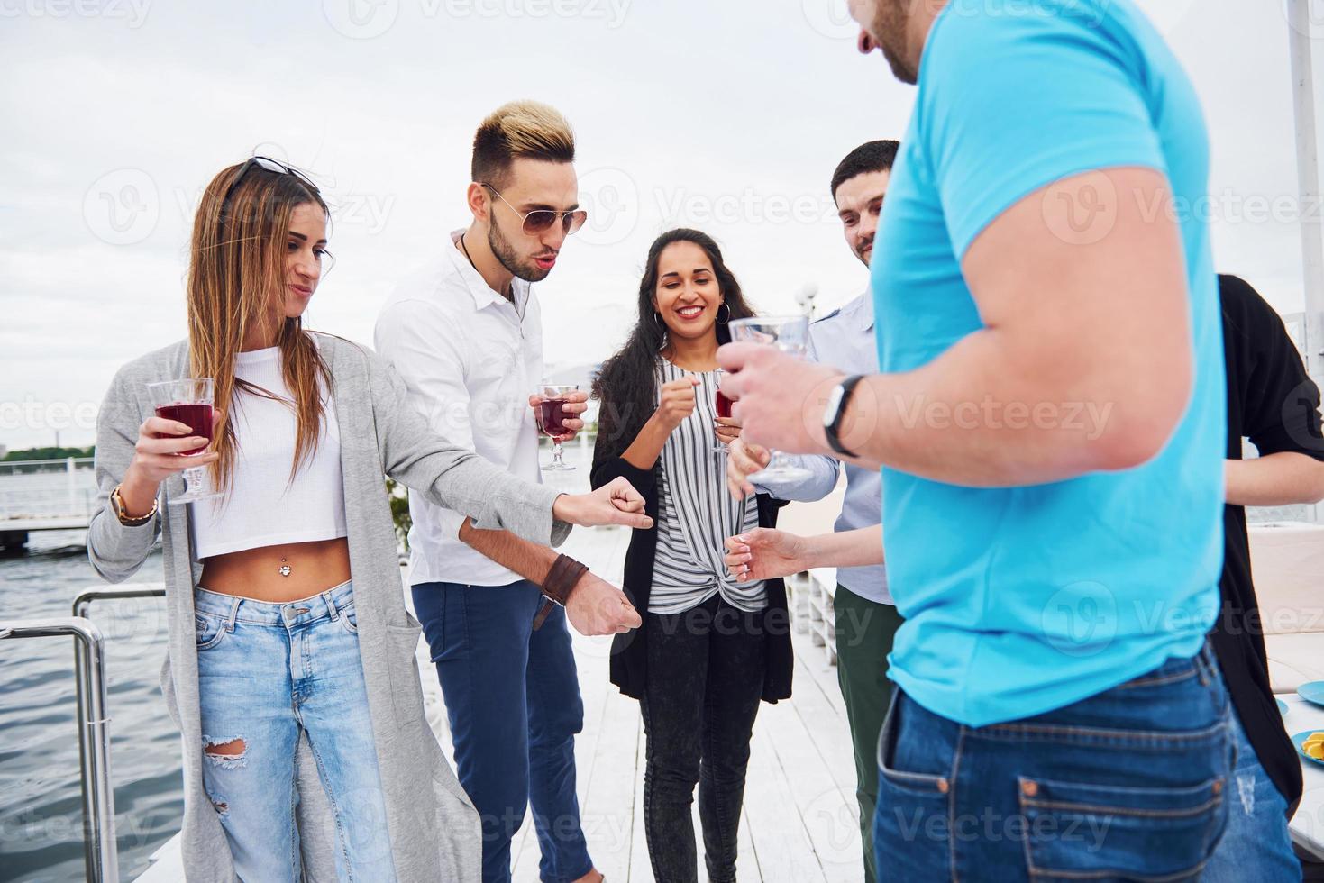 porträtt av en grupp ungdomar som sitter på kanten av piren, utomhus i naturen. vänner njuter av ett spel på sjön. foto