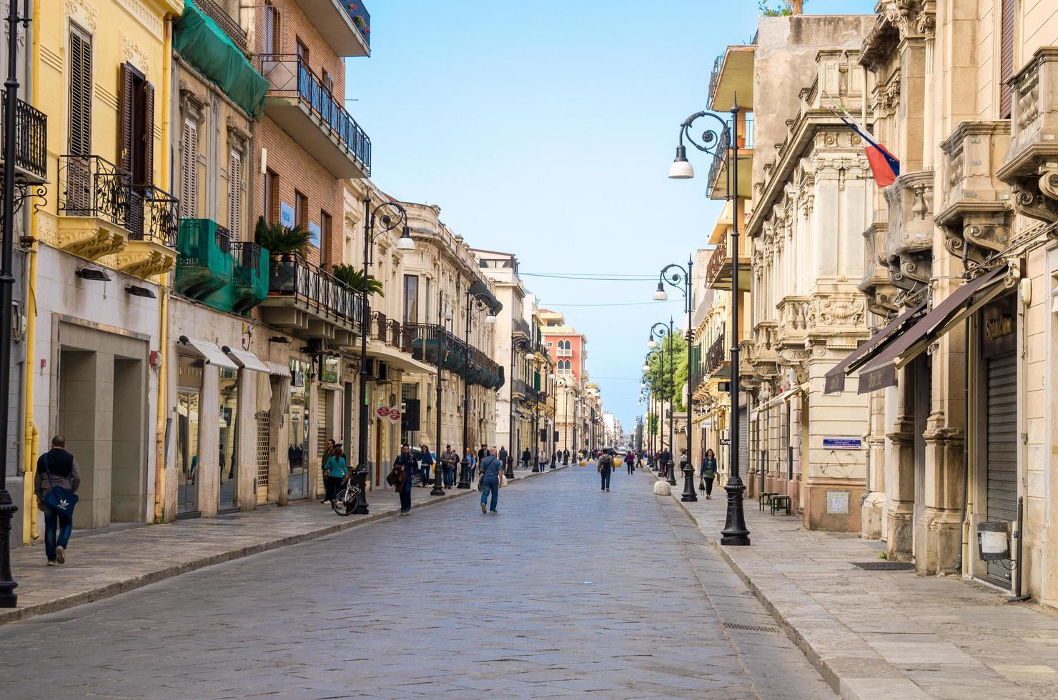 Italien, Reggio di Calabria, 11 maj 2018 gåturistgatan corso giuseppe garibaldi med gamla traditionella typiska byggnader, lampor och gröna träd i stadens historiska centrum foto